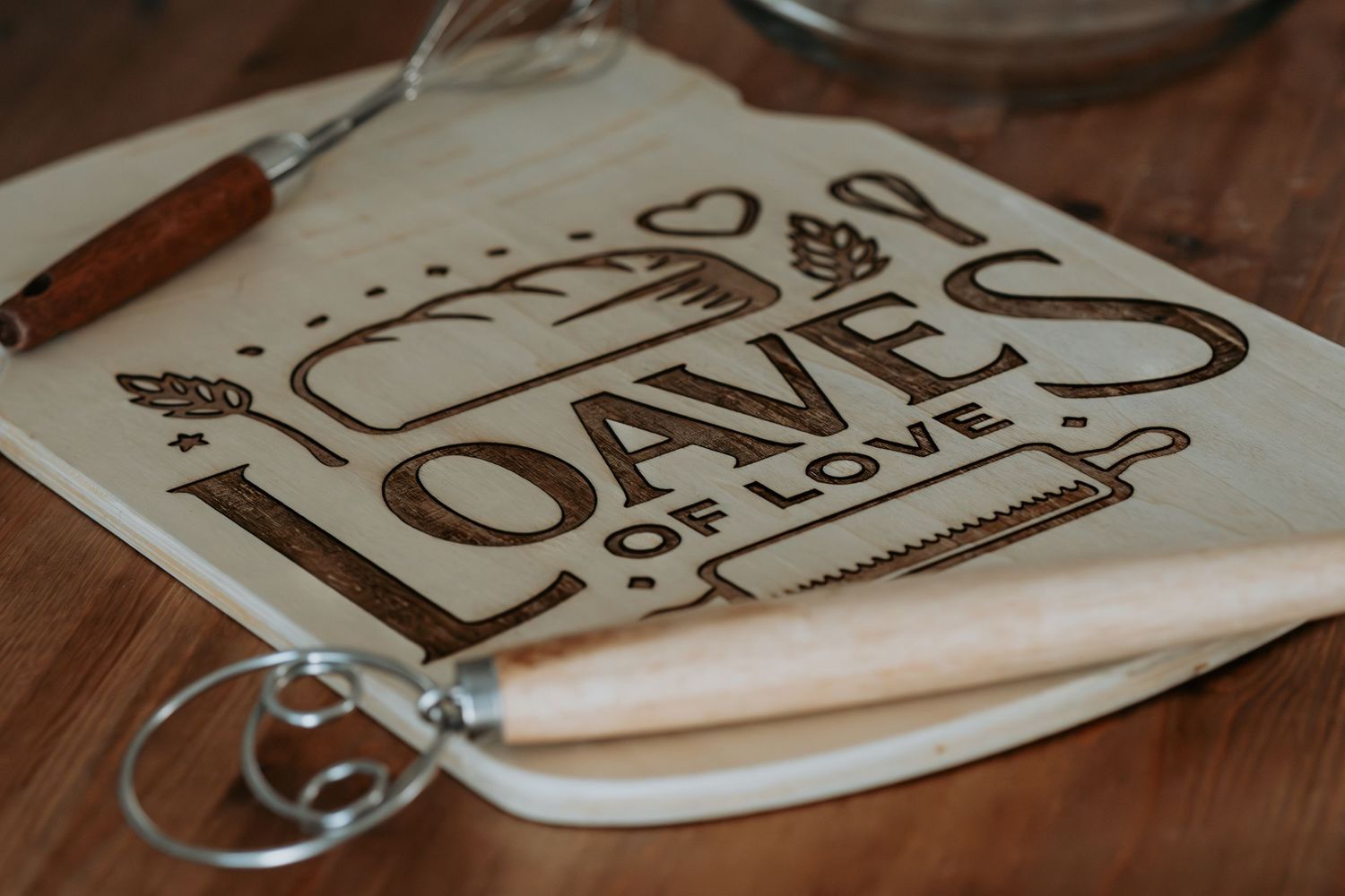 Wooden cutting boards with laser engraved designs and text are arranged on a dark wooden surface.