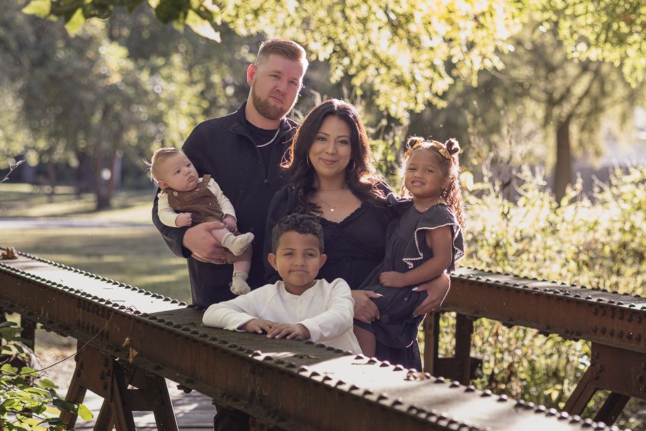 A family sits together on a wooden bench in a sunlit park reading books and spending quality time outdoors.