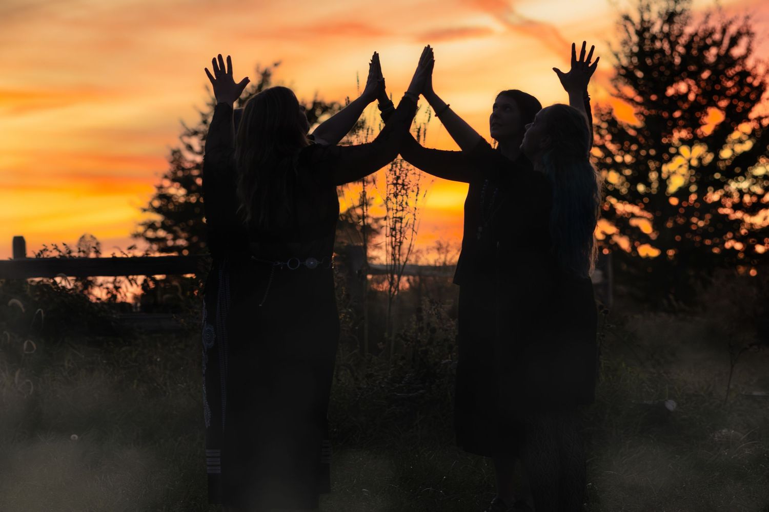Silhouettes of people with raised hands against a vibrant orange sunset sky.