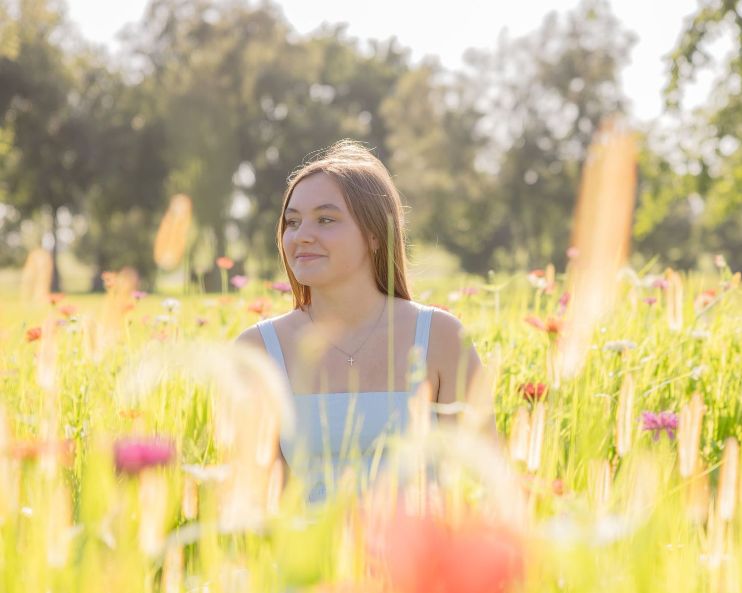 Young woman sitting peacefully in a sunny wildflower meadow with colorful blooms surrounding her.