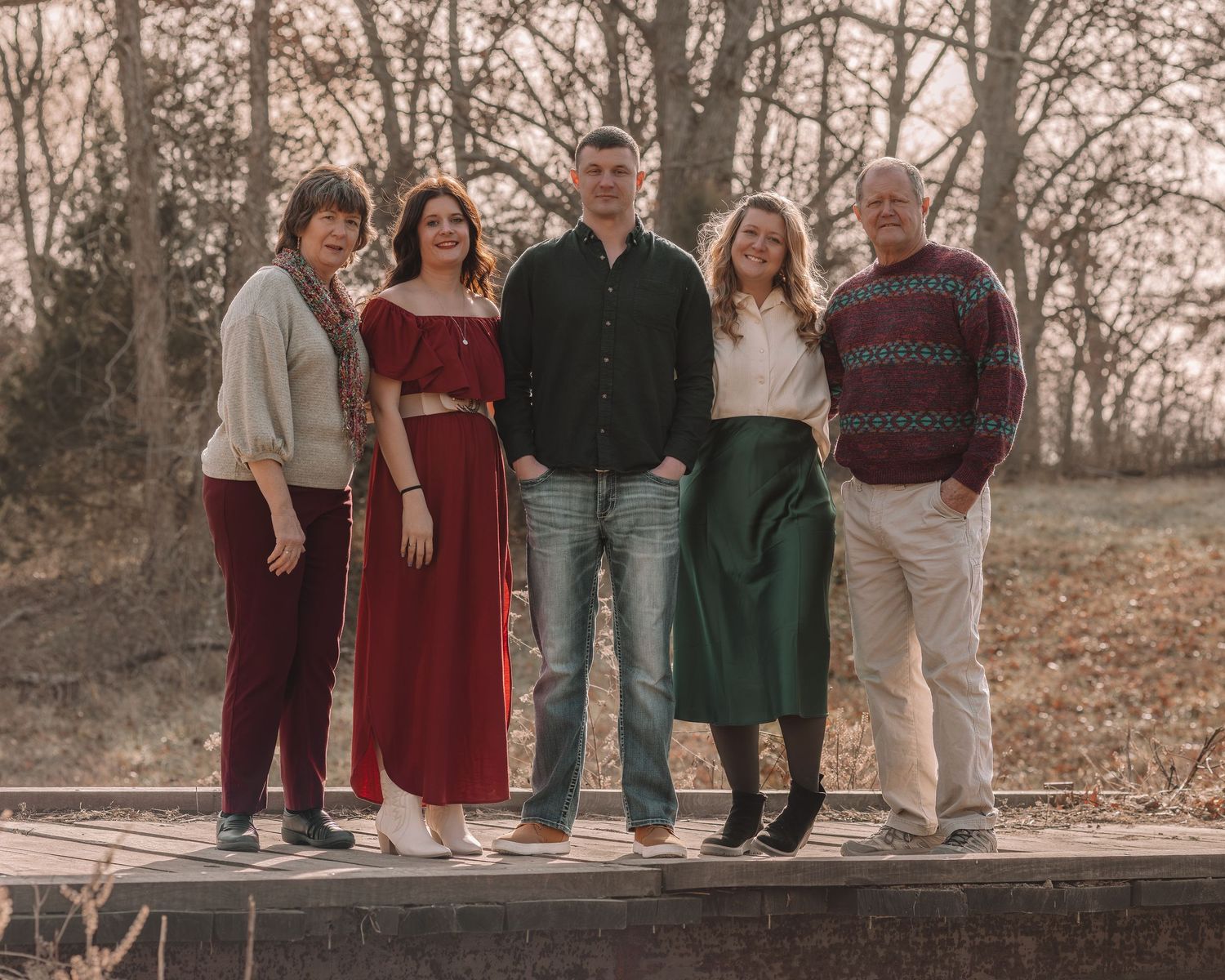 A group in coordinating burgundy and green outfits poses together in a wooded outdoor setting during autumn.