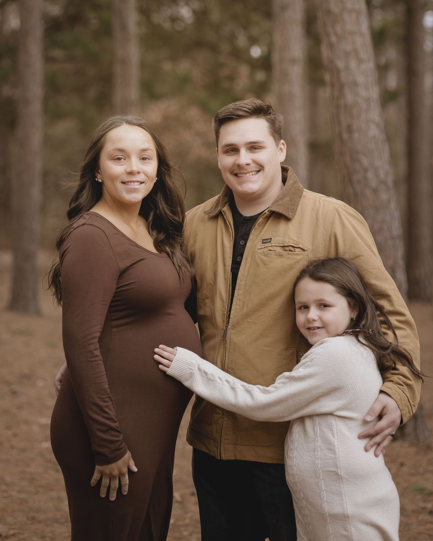 Family sharing intimate moments together in a wooded forest setting wearing coordinated brown and tan outfits.