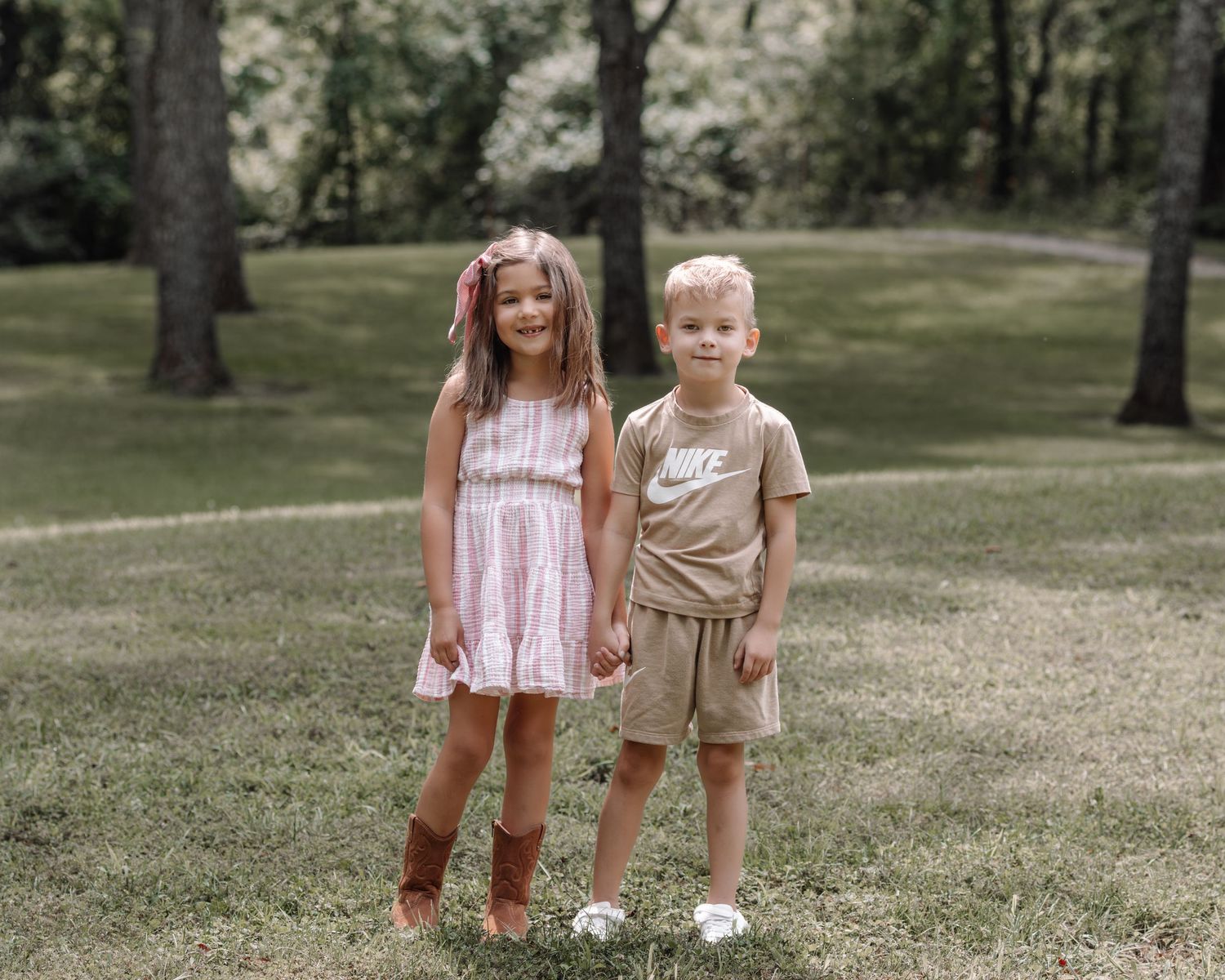Two small children stand together on grass during a summer outdoor photoshoot with rustic props.