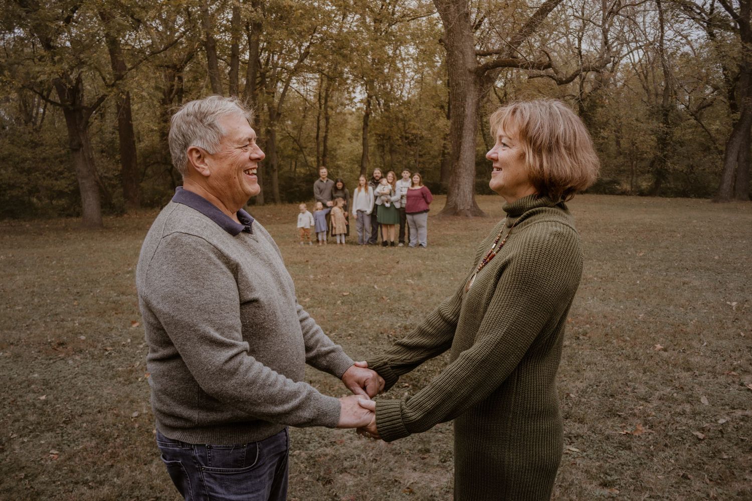 Multi-generational family gathering for photos in a park during fall season.