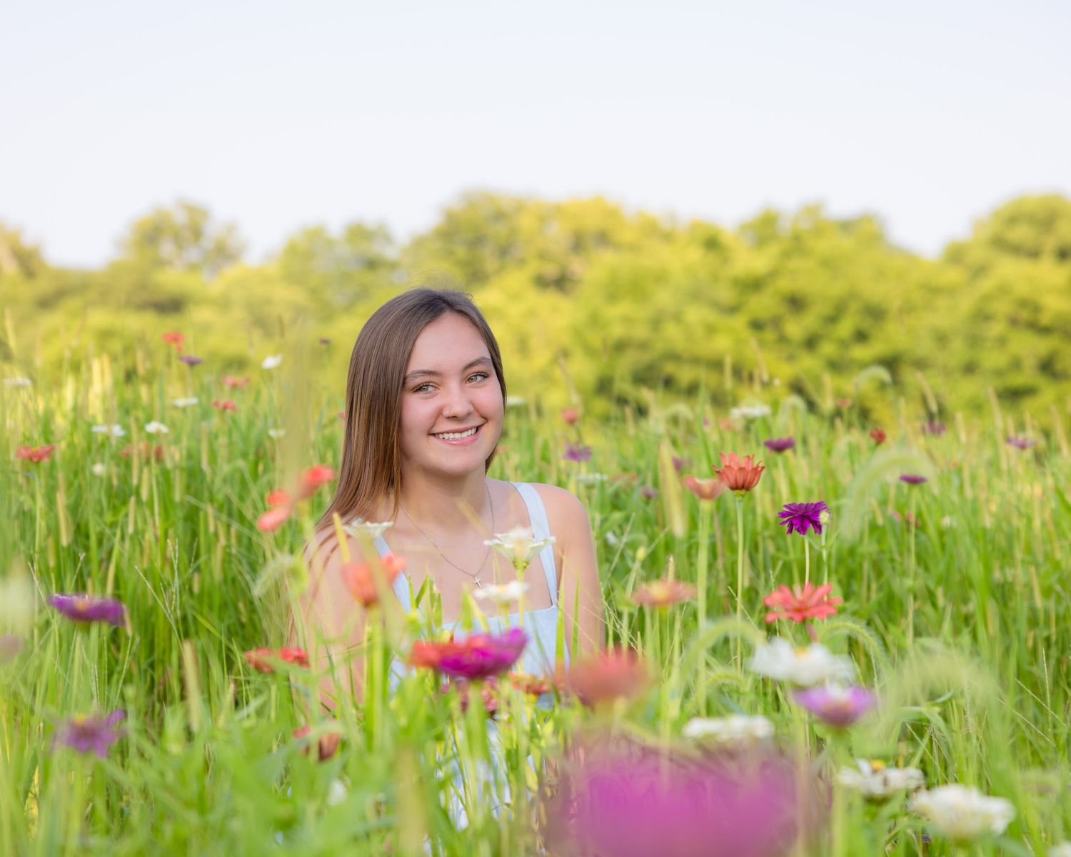 Smiling young woman sitting in a vibrant wildflower meadow with colorful blooms and lush green grass.