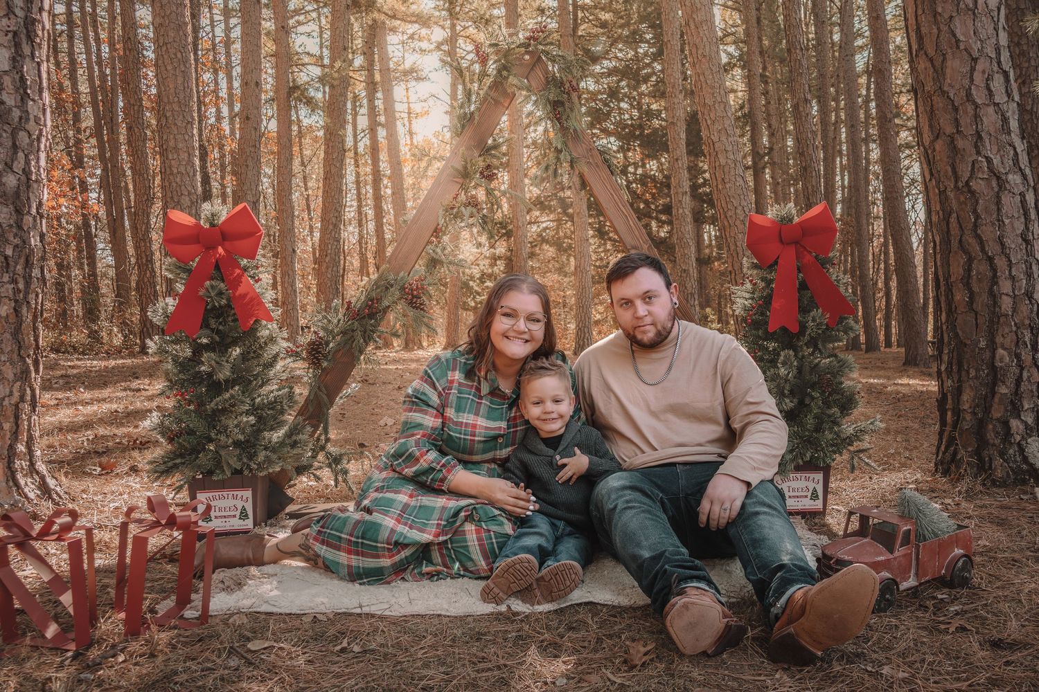 Family poses together in a cozy winter forest setting with festive red poinsettias and plaid blankets.