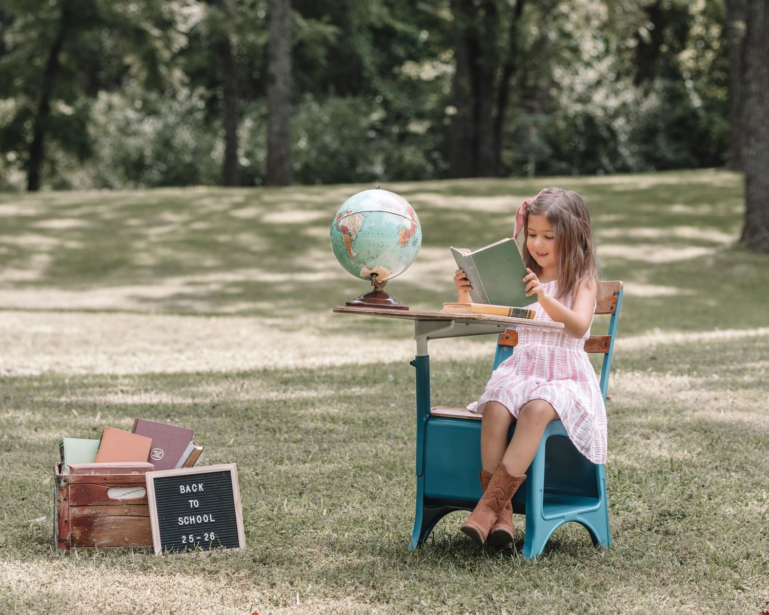 A back-to-school themed outdoor photography setup with a small desk and educational props on grass.