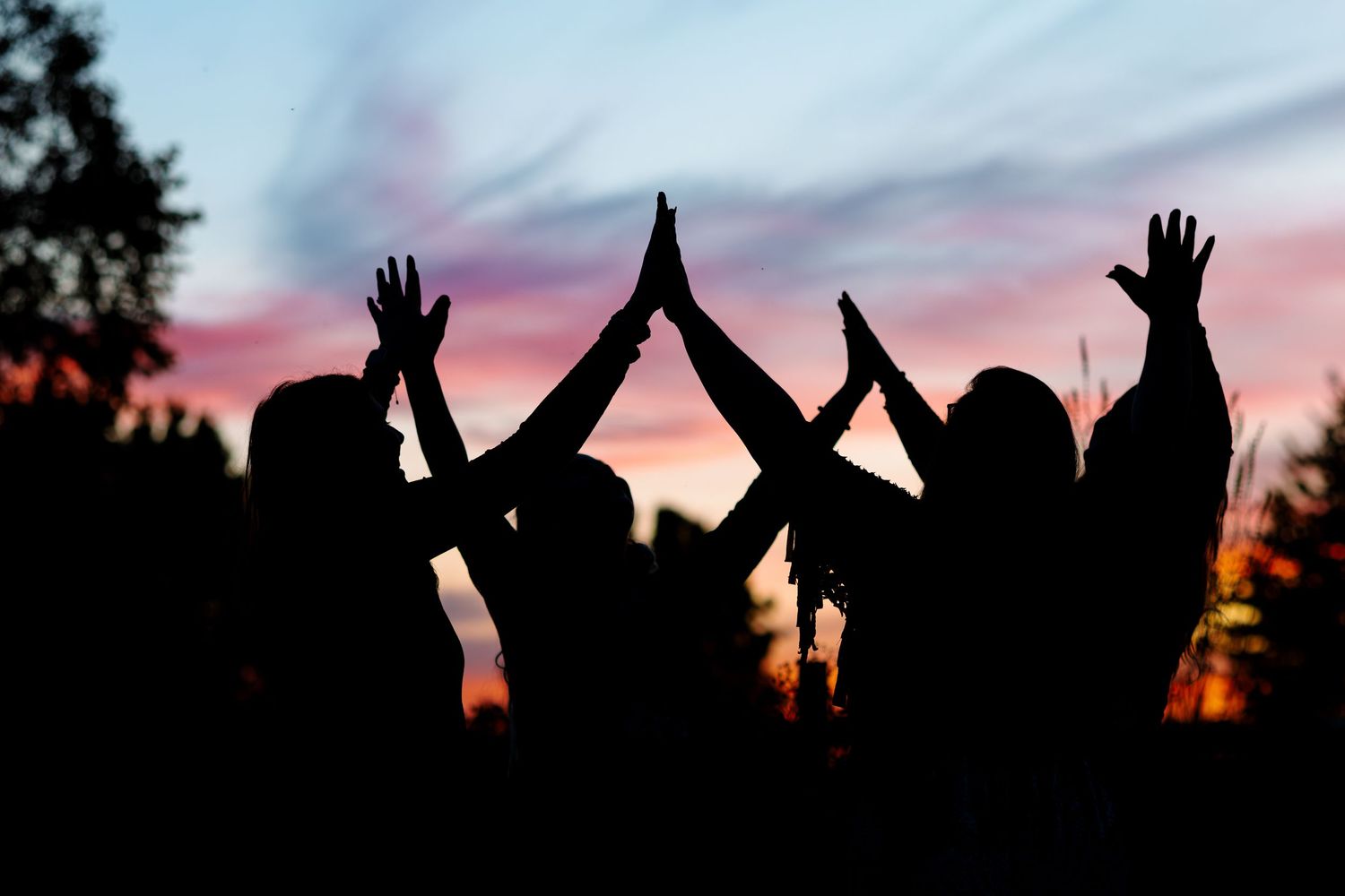 Silhouettes of raised hands against a colorful sunset sky.