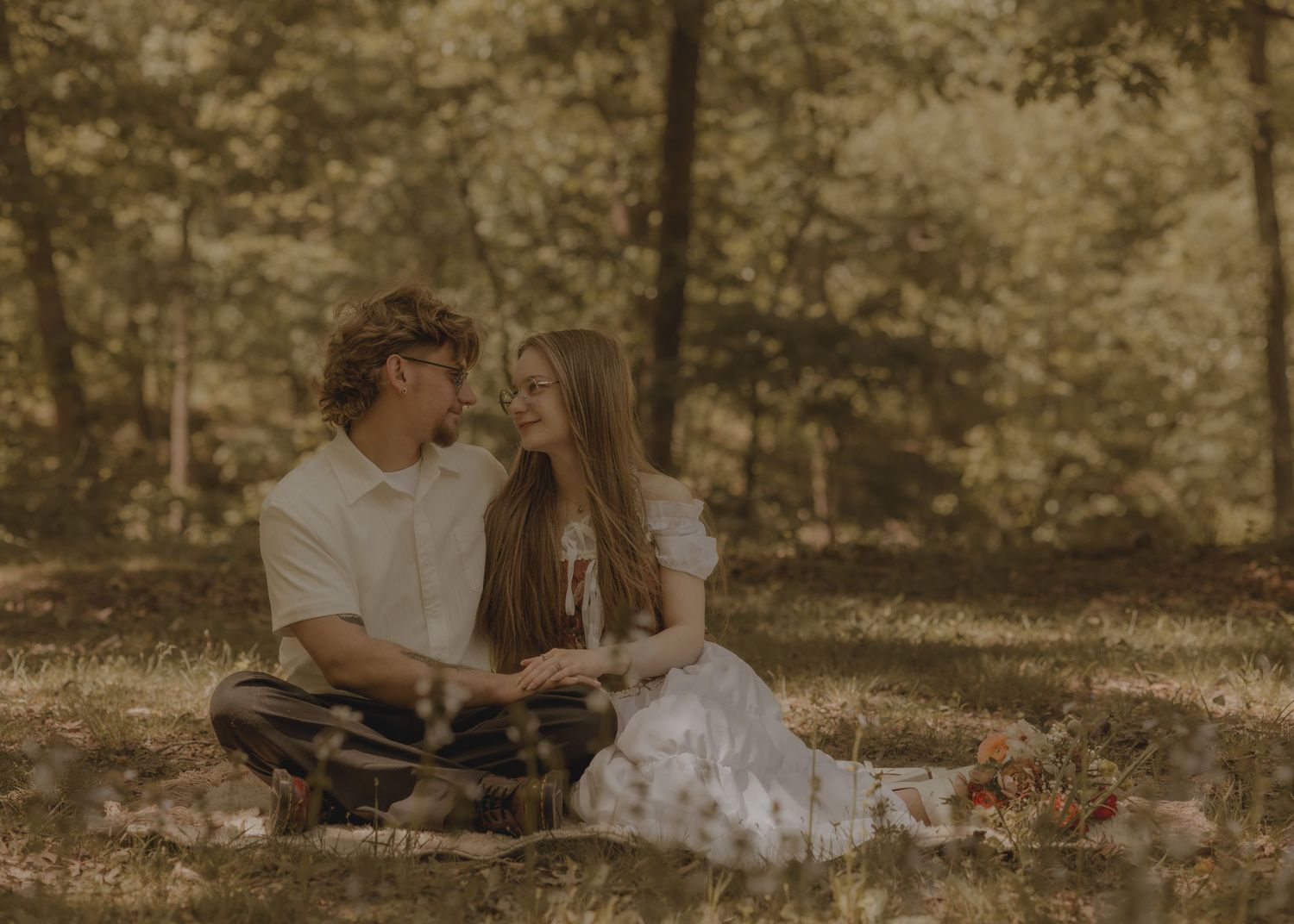 Romantic couple sitting together in a sunlit forest, sharing an intimate moment on the grass.