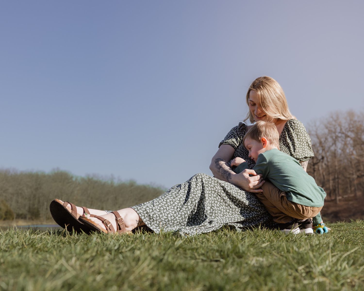Woman in floral dress relaxing on grass with child in casual outdoor setting.