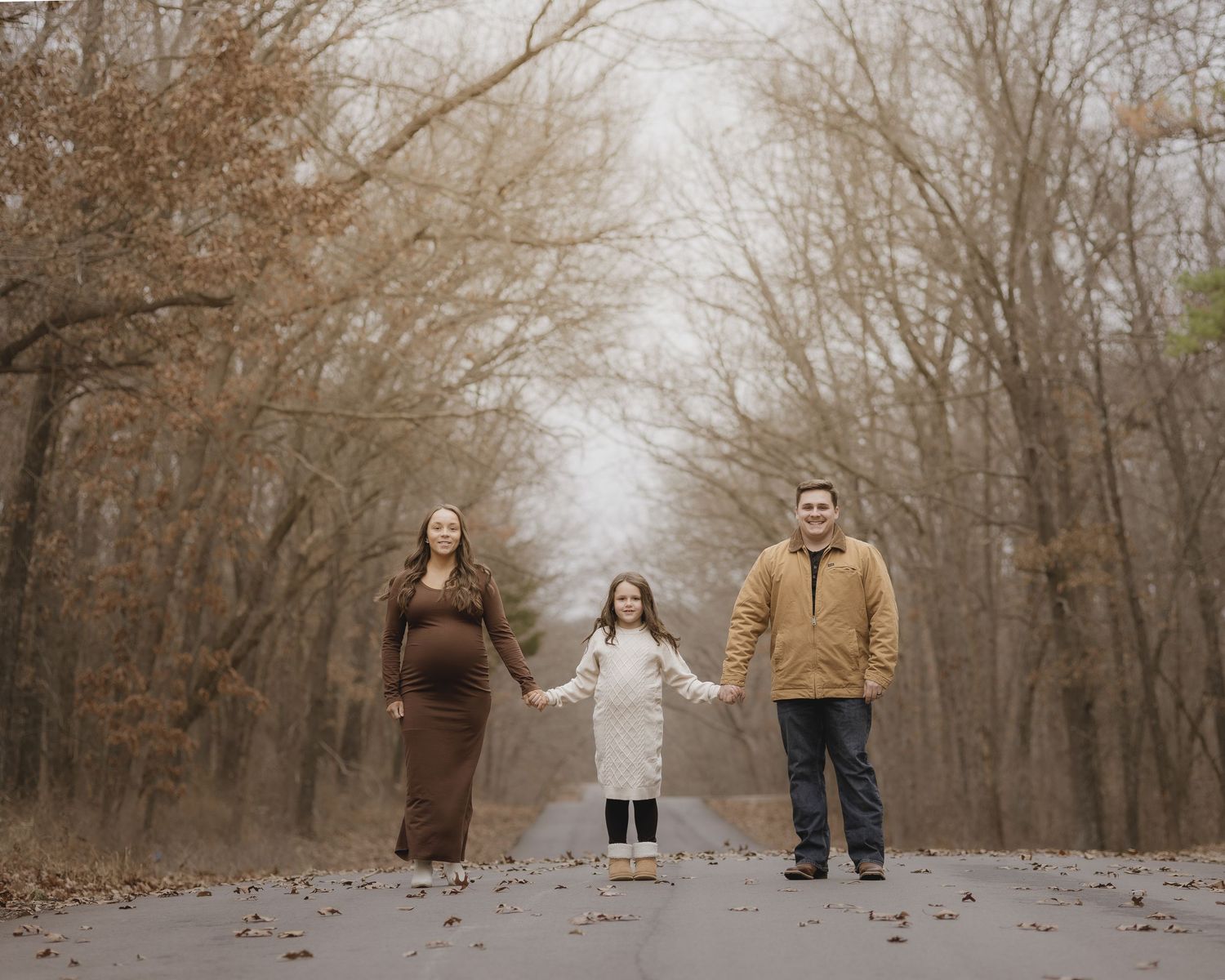 A family stands together in a wooded path during autumn with bare trees and fallen leaves creating a moody atmosphere.