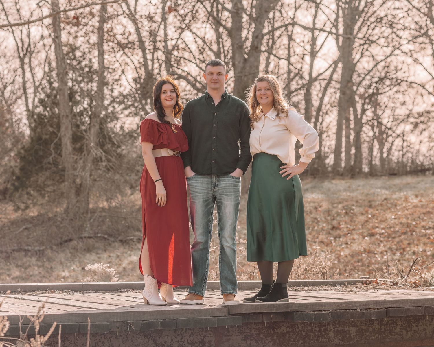 Family group arranged in casual poses on wooden fence with fall foliage and trees in background.