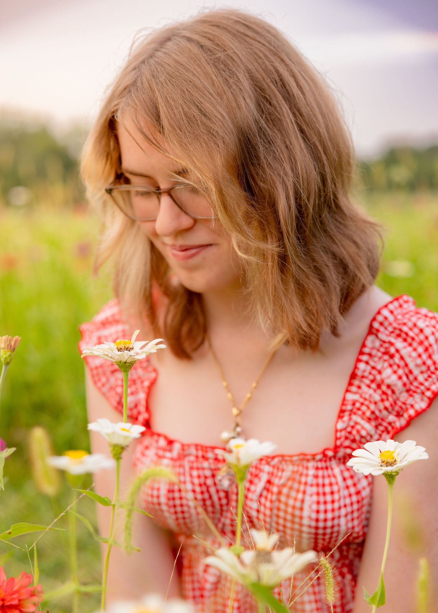 Young woman in red gingham dress smelling white daisies in a sunny flower field.