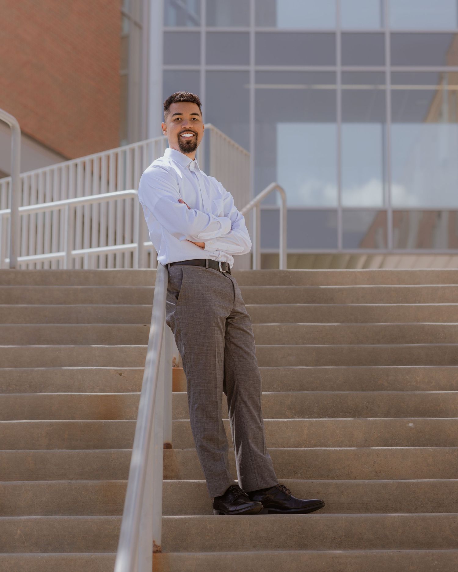 Young man in white dress shirt and gray slacks posing confidently on university steps.