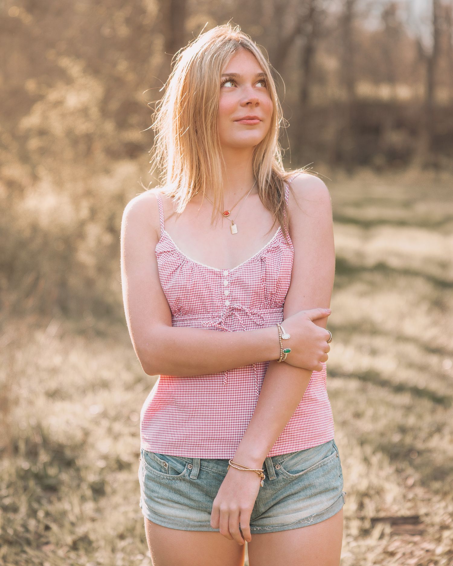 Young blonde woman in pink top and denim shorts posing in sunny field.
