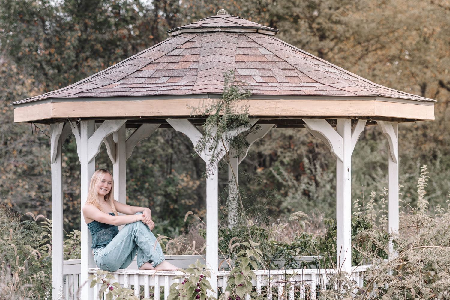 White wooden gazebo with ornate trim stands elegantly in a garden setting surrounded by trees and greenery.