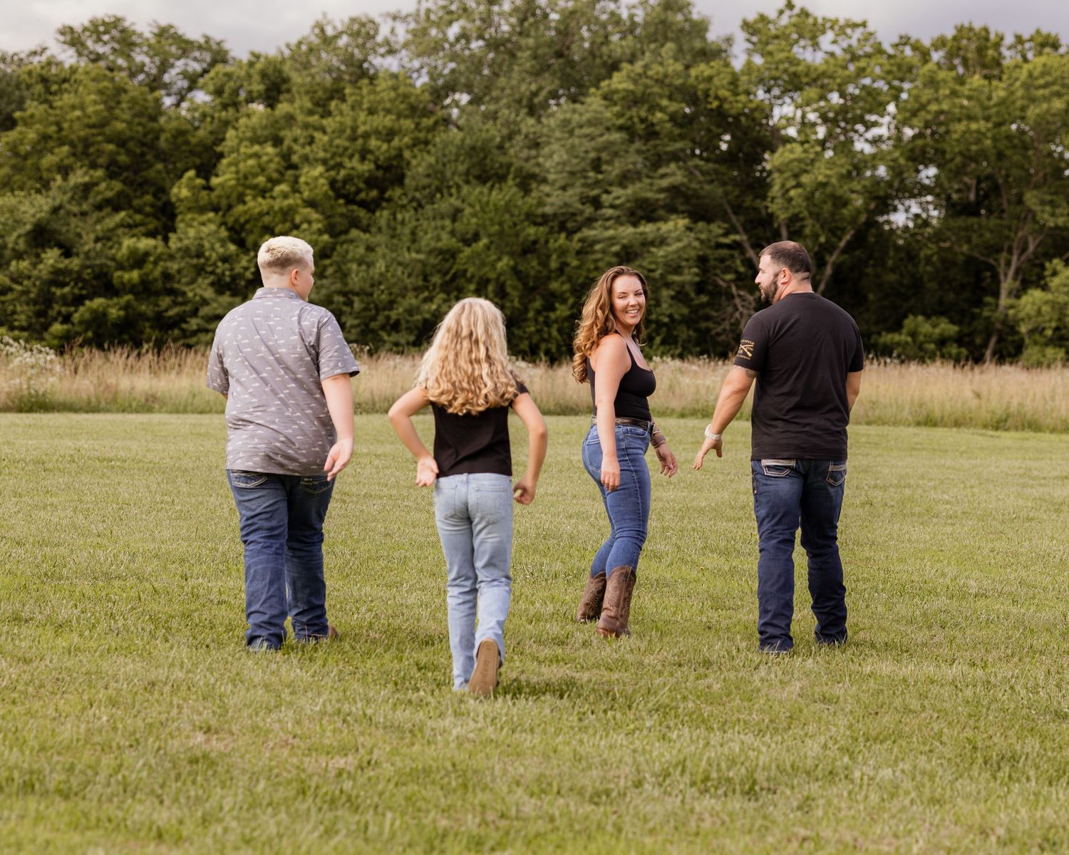 Four people walking in a lush green field with trees in the background on a cloudy day.