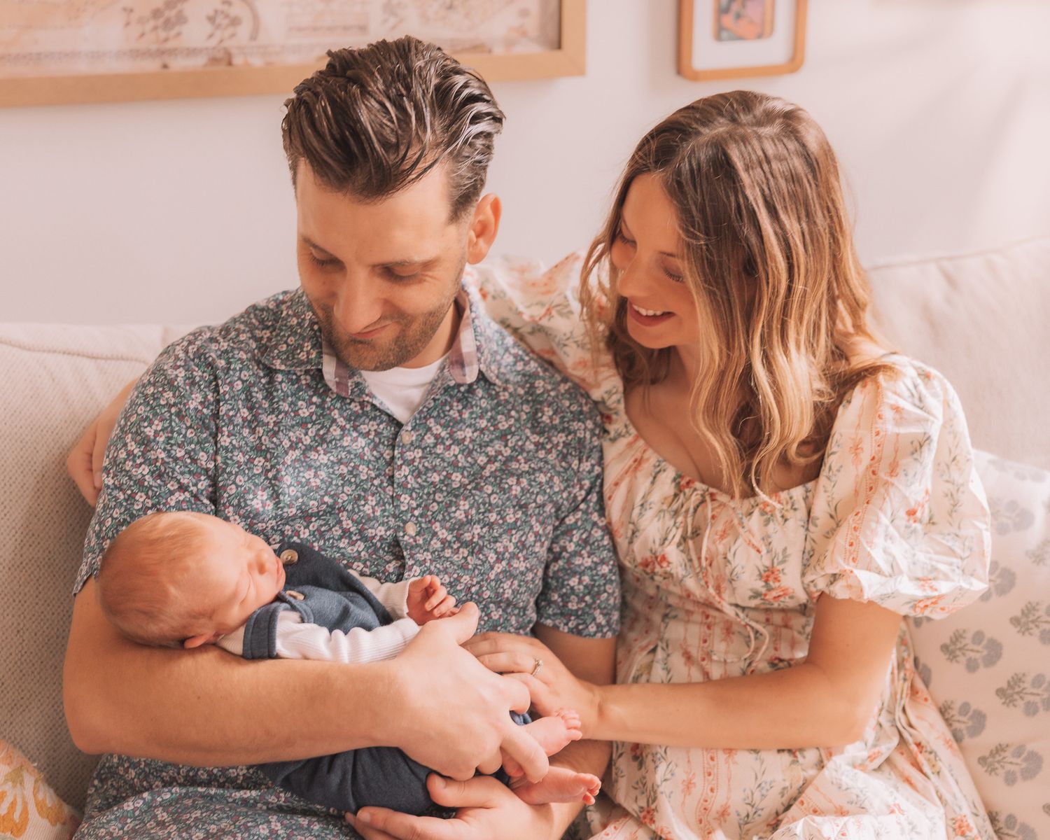 Happy couple sitting together on a sofa, lovingly looking at their newborn baby in a bright room.
