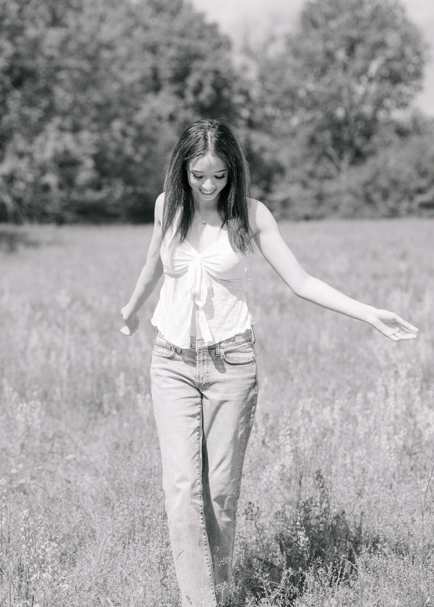 Black and white photo of a young woman in jeans and white top walking through a sunny meadow.