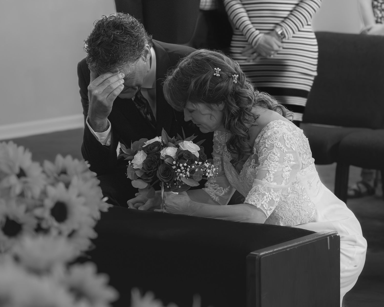 Black and white photo of emotional bride and groom praying together at altar during wedding ceremony.