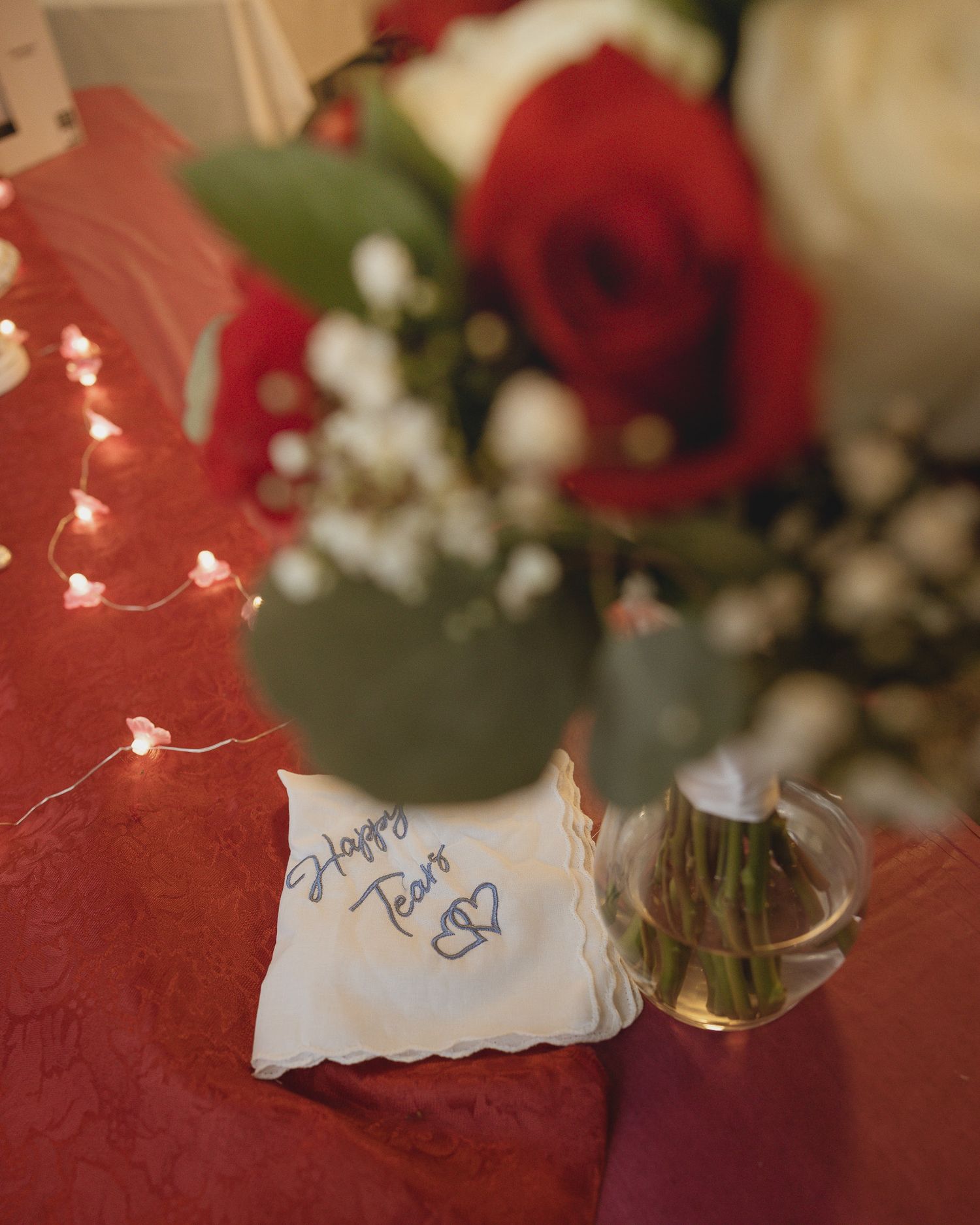 A handwritten note with a heart drawing sits beside a red rose and baby's breath flowers on a red surface.