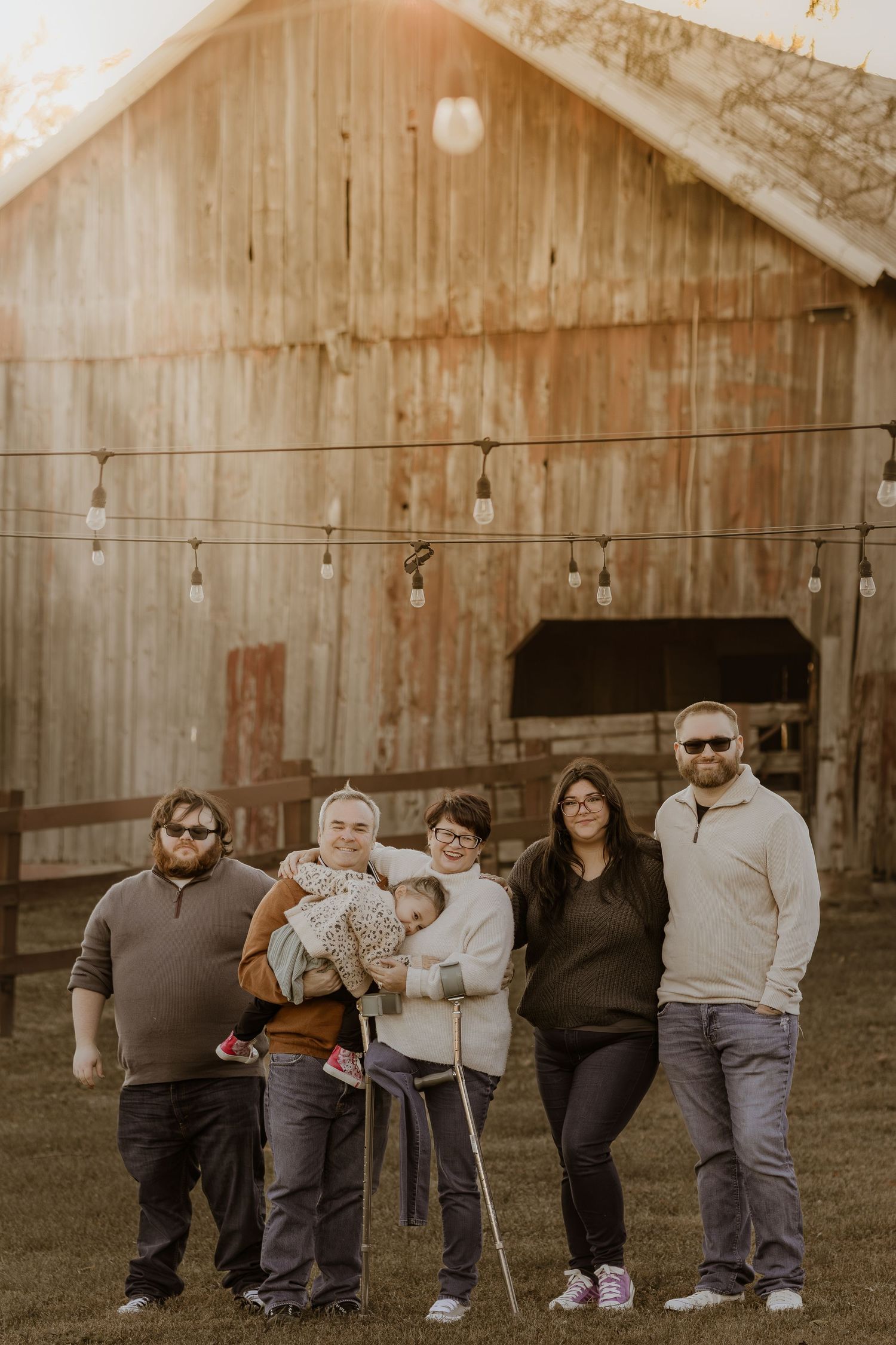 Family members sit together in a row against a rustic wooden barn wall during an outdoor photo session.