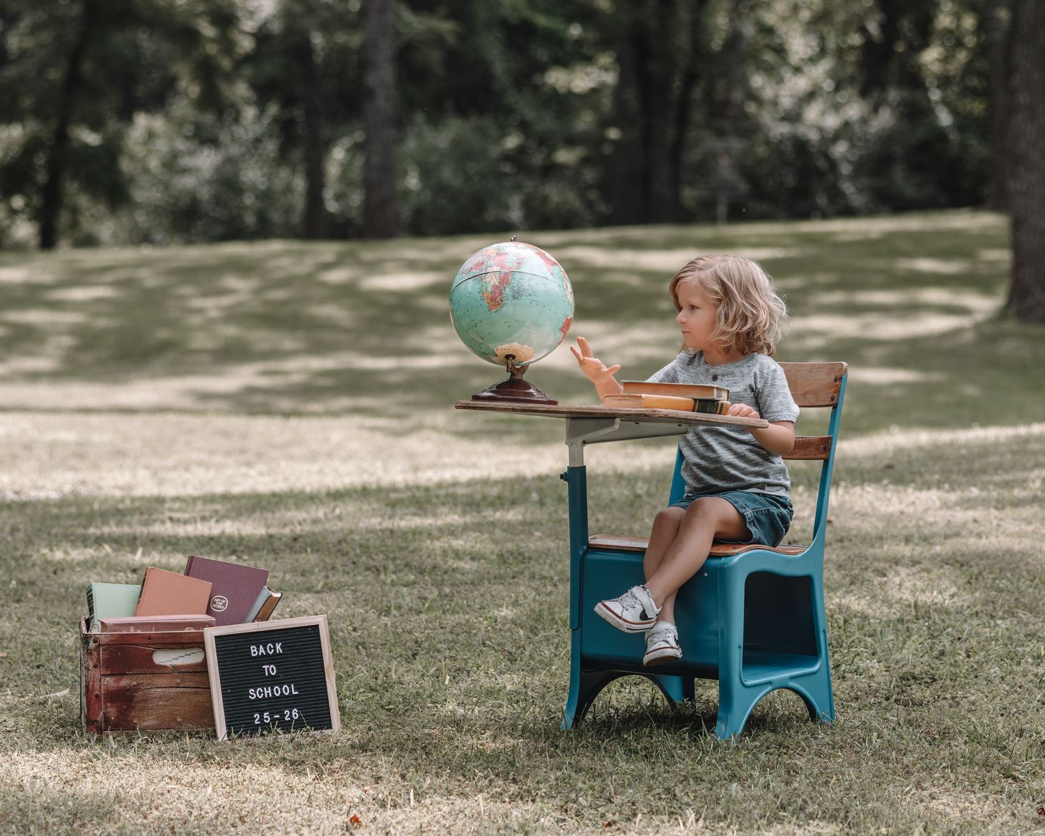 Children play with a globe and toy car in a sunny park setting with vintage-inspired props and decor.
