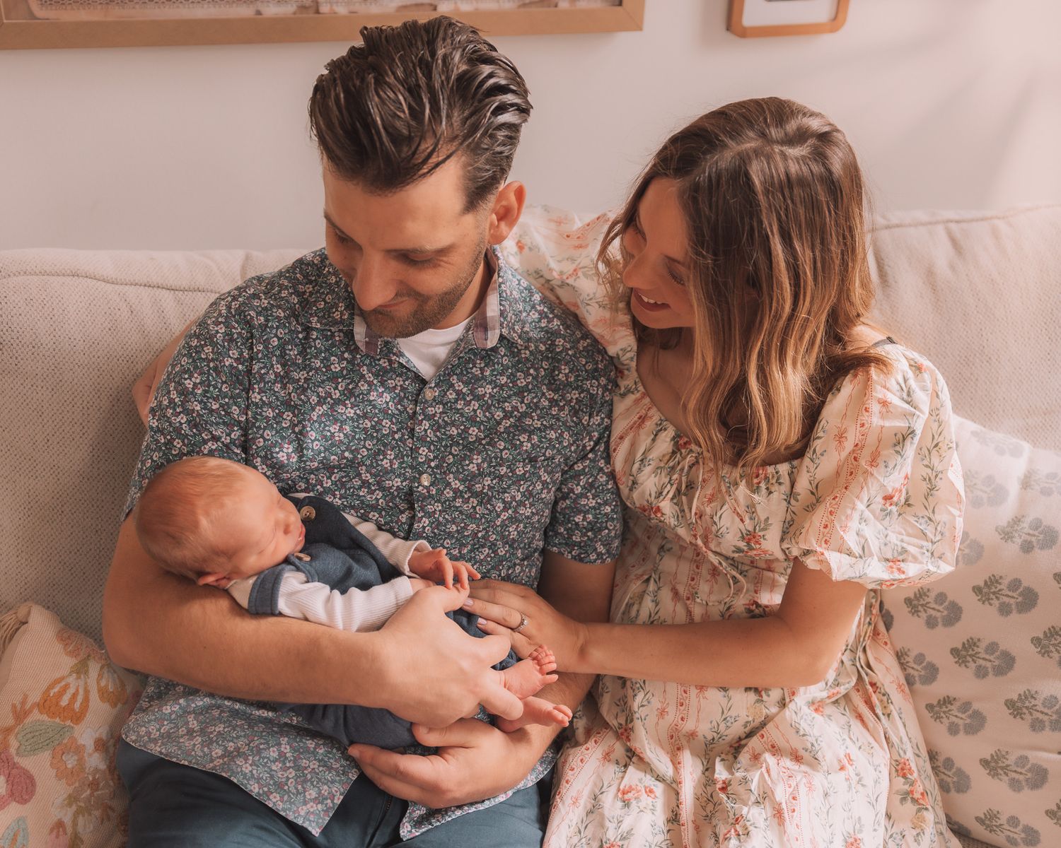 A happy couple smiling and bonding with their newborn baby while sitting on a couch together.