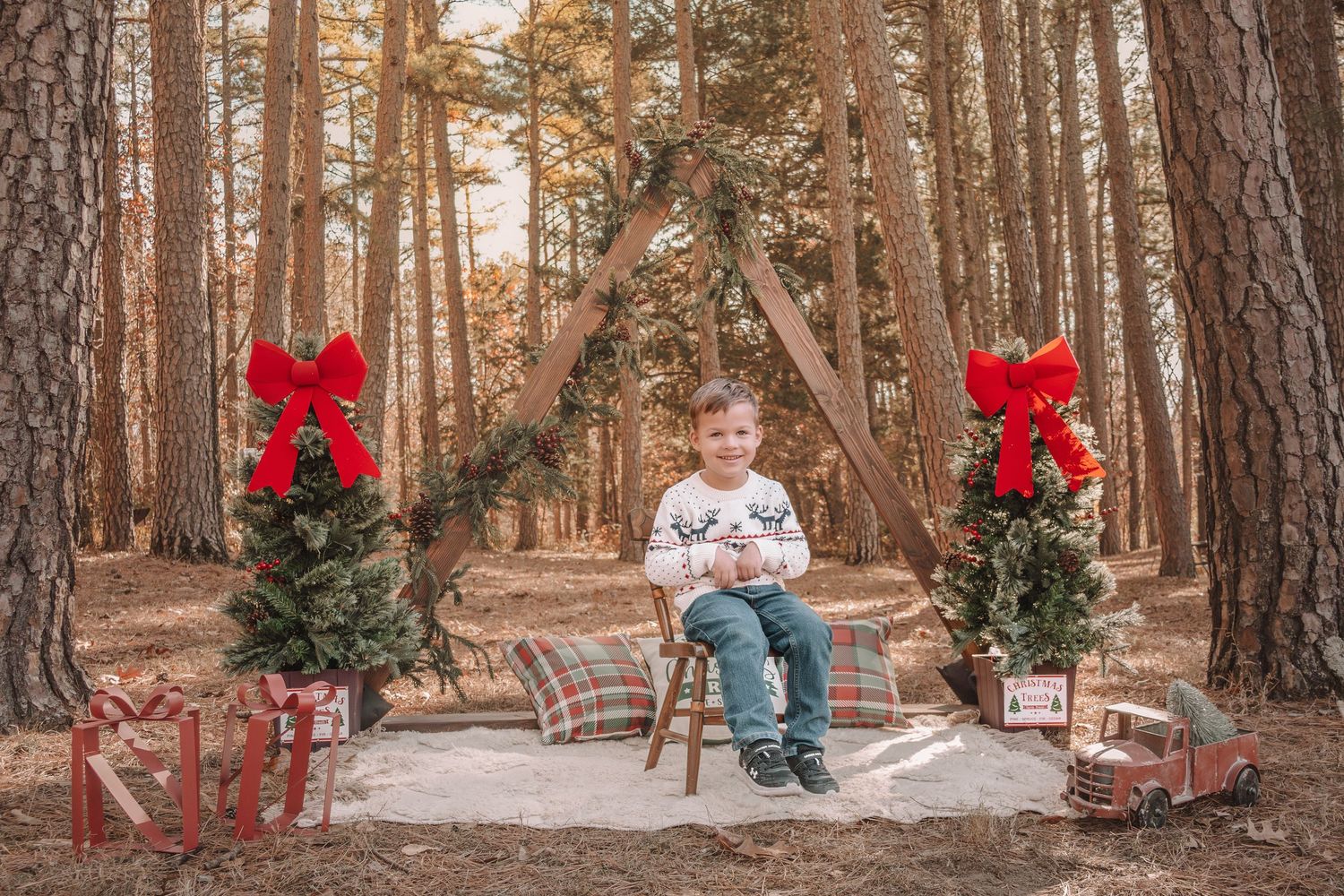 A festive holiday scene in a pine forest with two small decorated Christmas trees adorned with red bows and wrapped presents.
