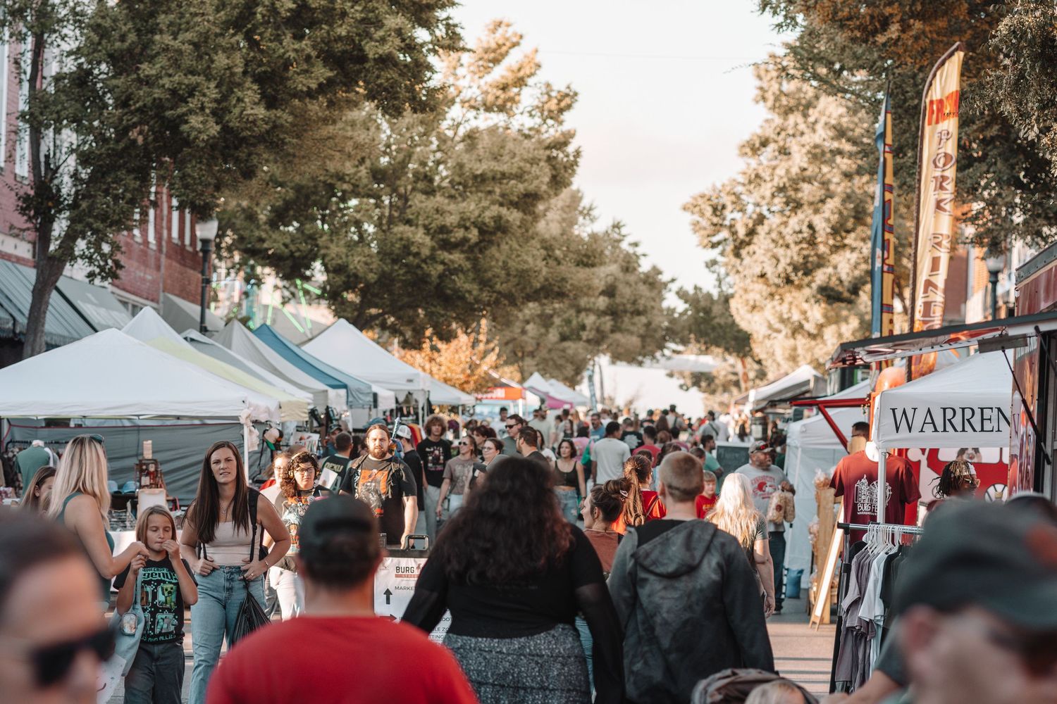 Large crowd gathered at an outdoor festival or street fair during golden hour.