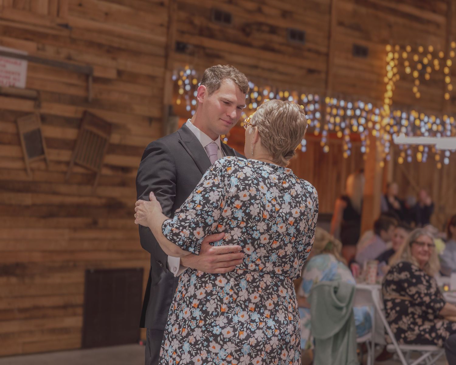 Couple sharing a romantic dance in a rustic barn venue decorated with string lights at a wedding reception.