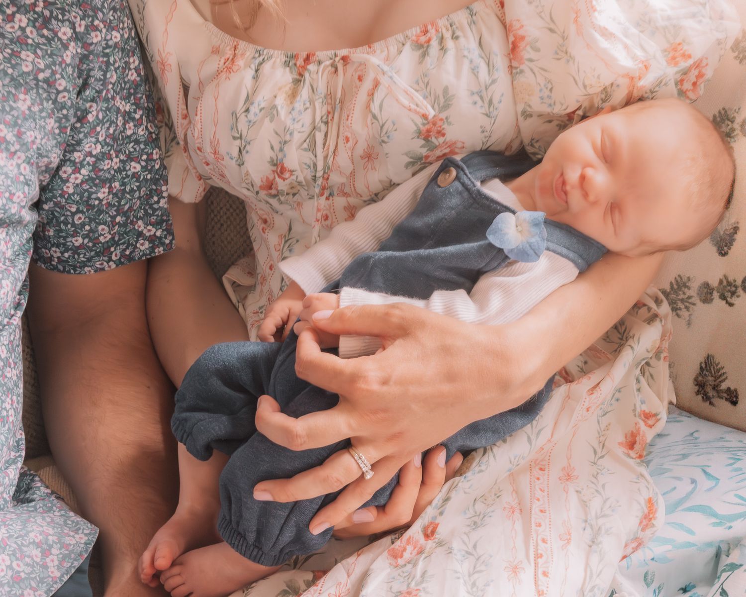 Parents cradling a sleeping newborn baby dressed in a blue outfit, captured from above in a tender moment.