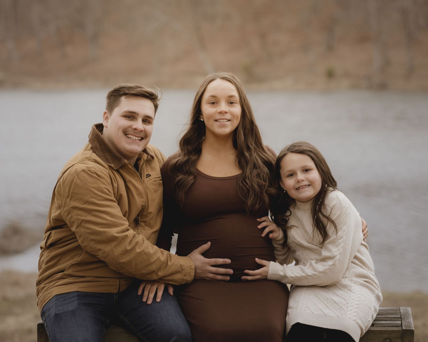 Family wearing brown and black outfits poses together outdoors during autumn photoshoot.