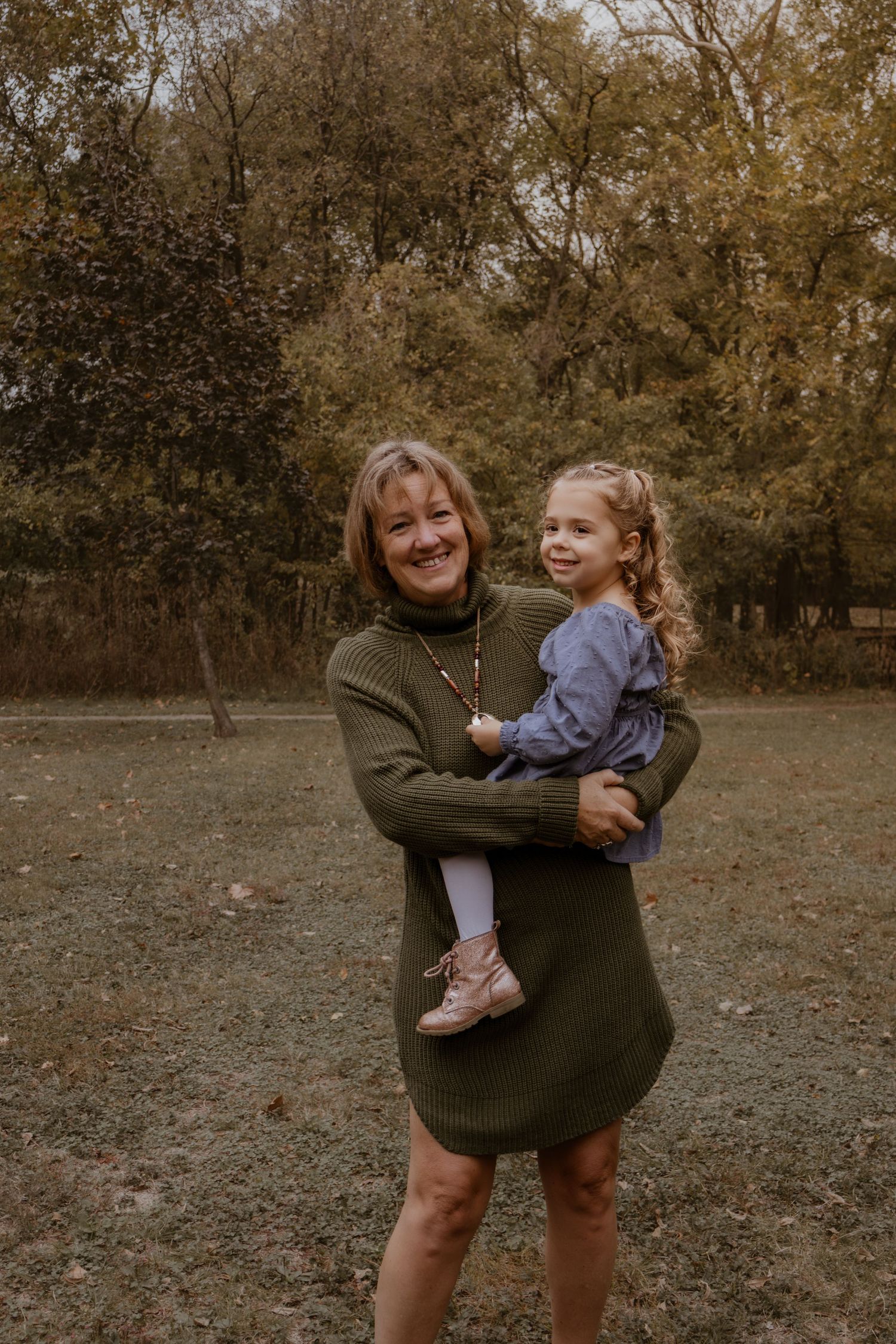 A heartwarming outdoor portrait of two people embracing and smiling in a wooded setting during autumn.
