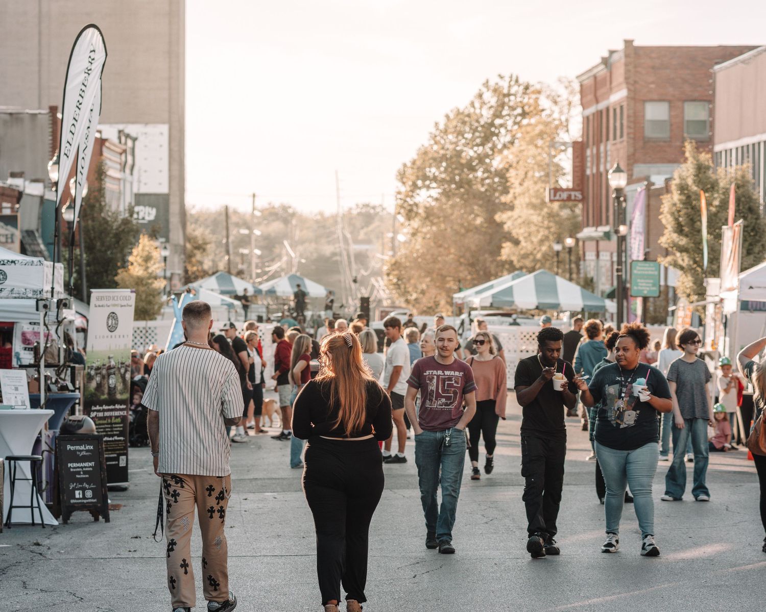 People walking along a city street lined with shops and buildings during sunset.
