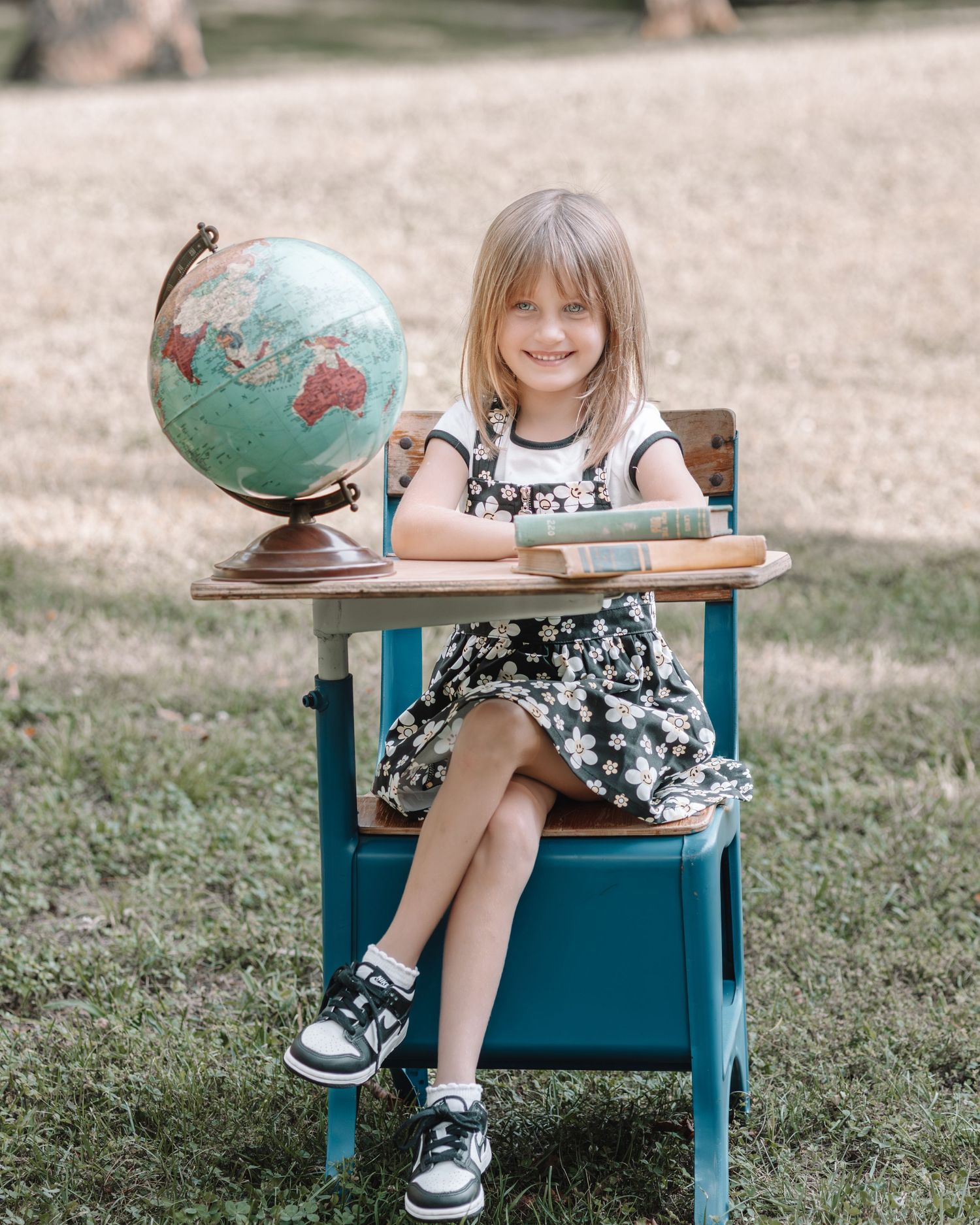 A student sits at a vintage school desk with a globe and books in an outdoor setting.