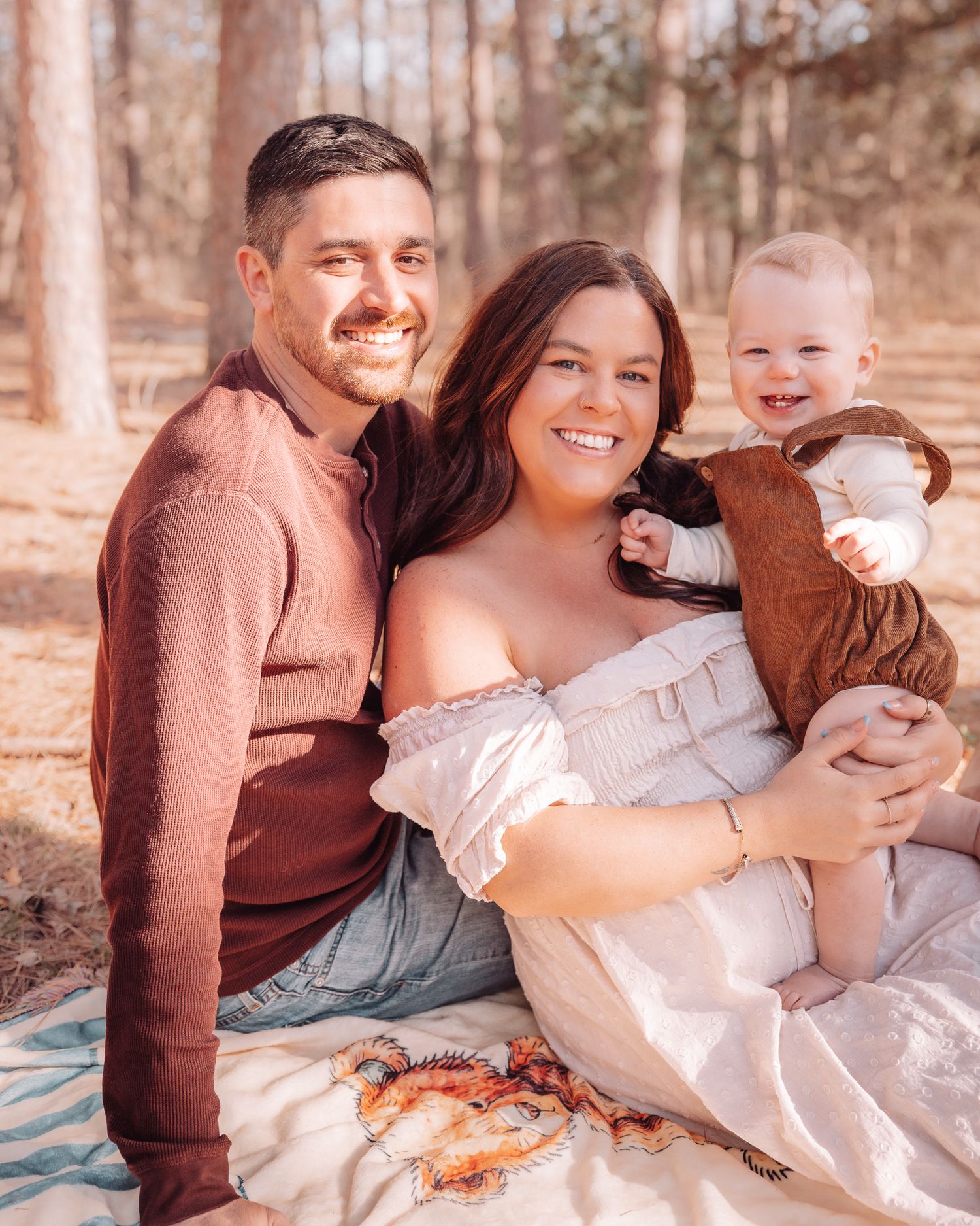 Family relaxes on blanket during outdoor autumn photoshoot in forest.
