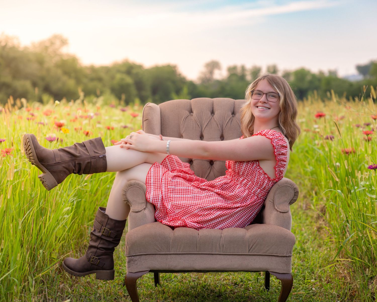 Young woman in red dress and brown boots sitting relaxed in armchair in a sunny wildflower meadow.