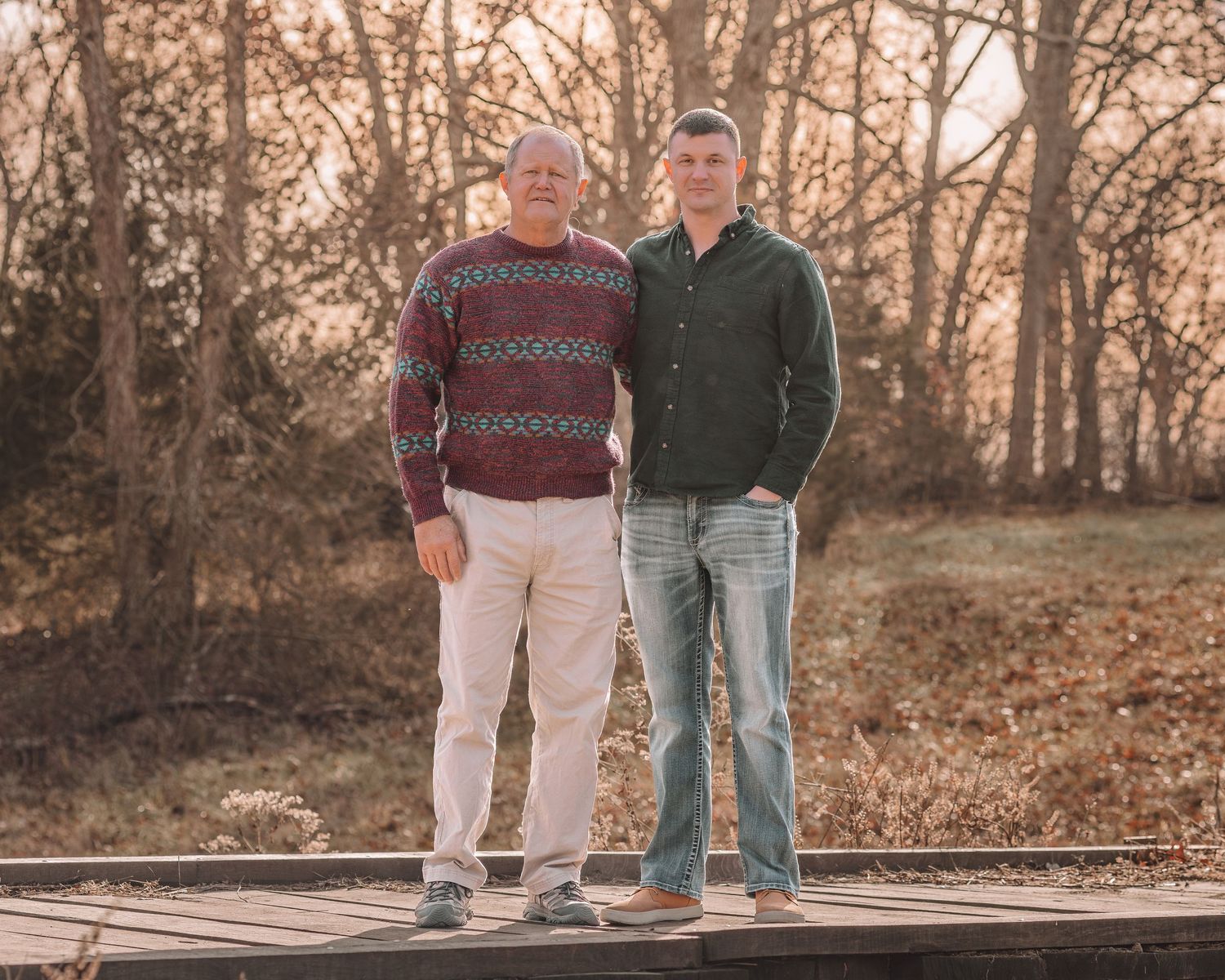 A couple in coordinating sweaters walks along a rustic wooden bridge at sunset during an autumn photo session.