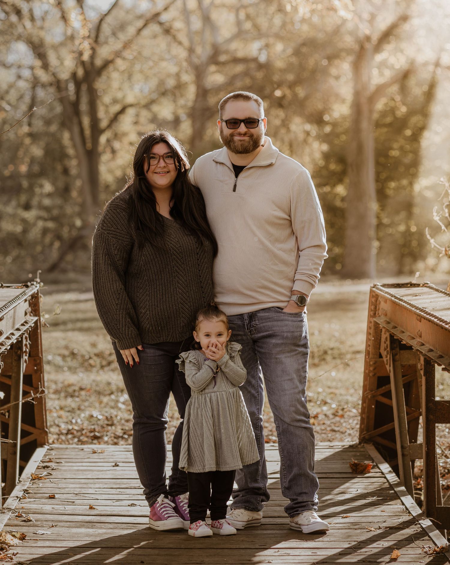 A family shares tender moments together on a wooden bridge during a golden sunset photo session.