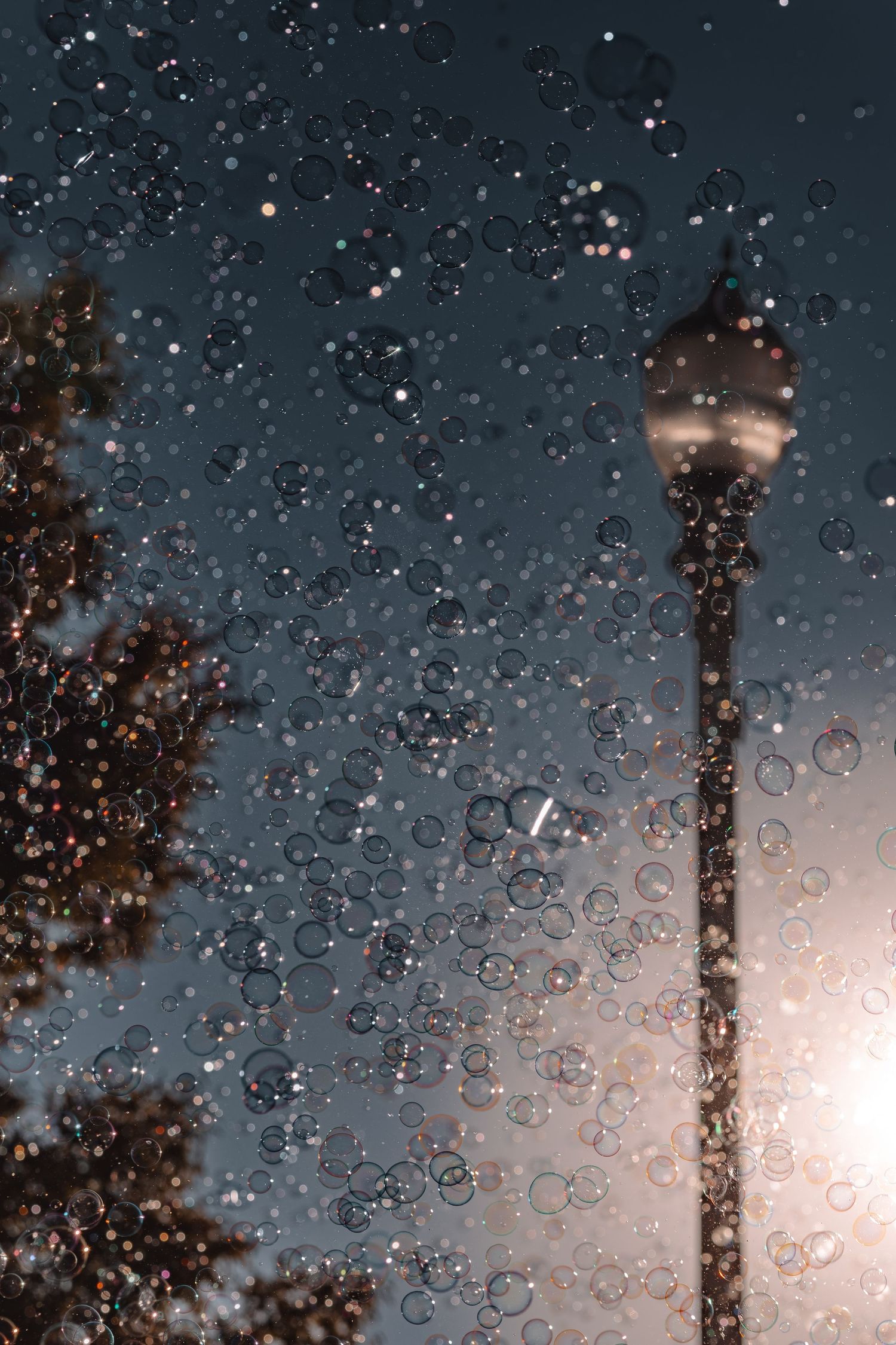 Raindrops on glass with a street lamp silhouetted against a moody evening sky.