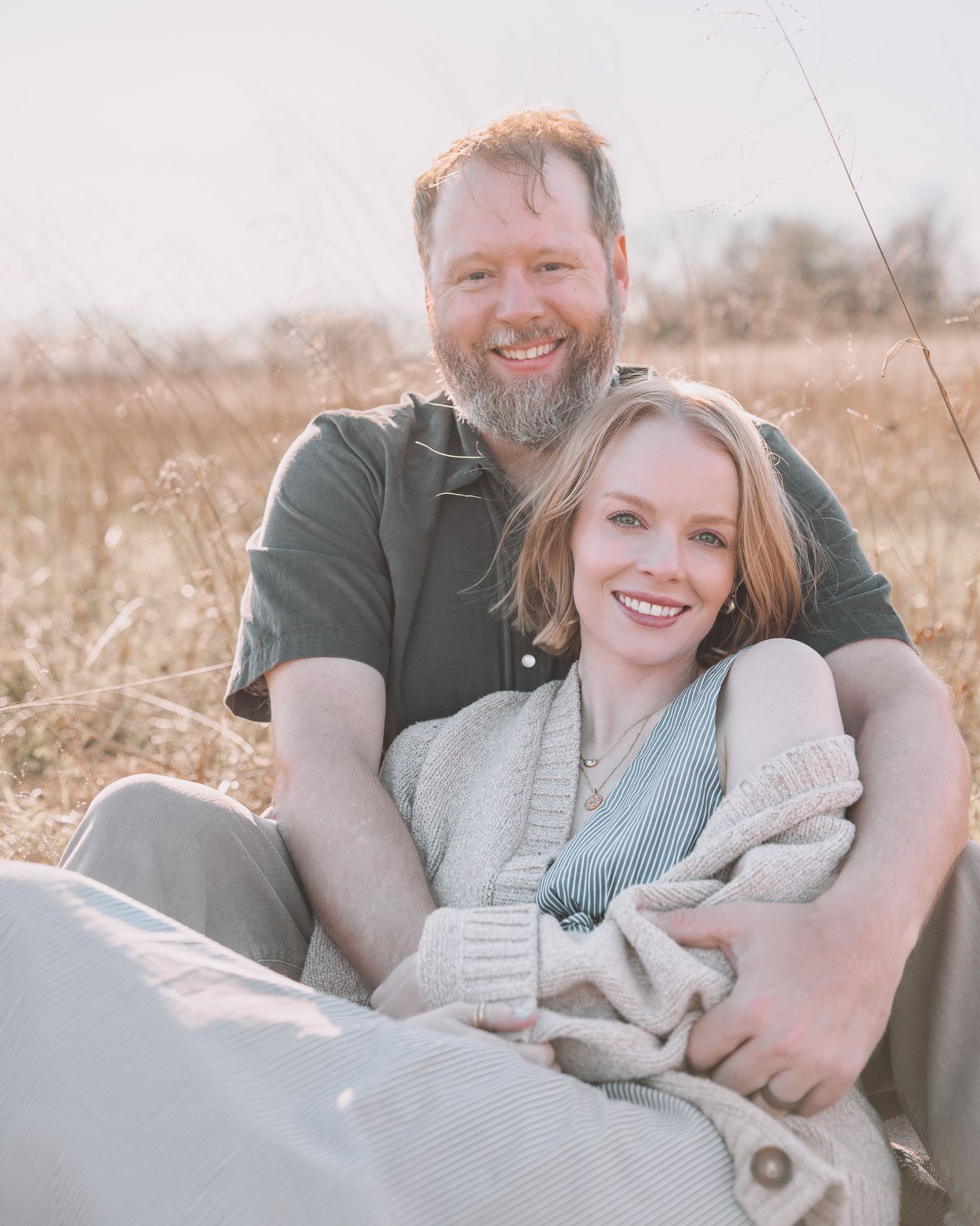 Smiling couple sitting together in a golden field enjoying a sunny day.