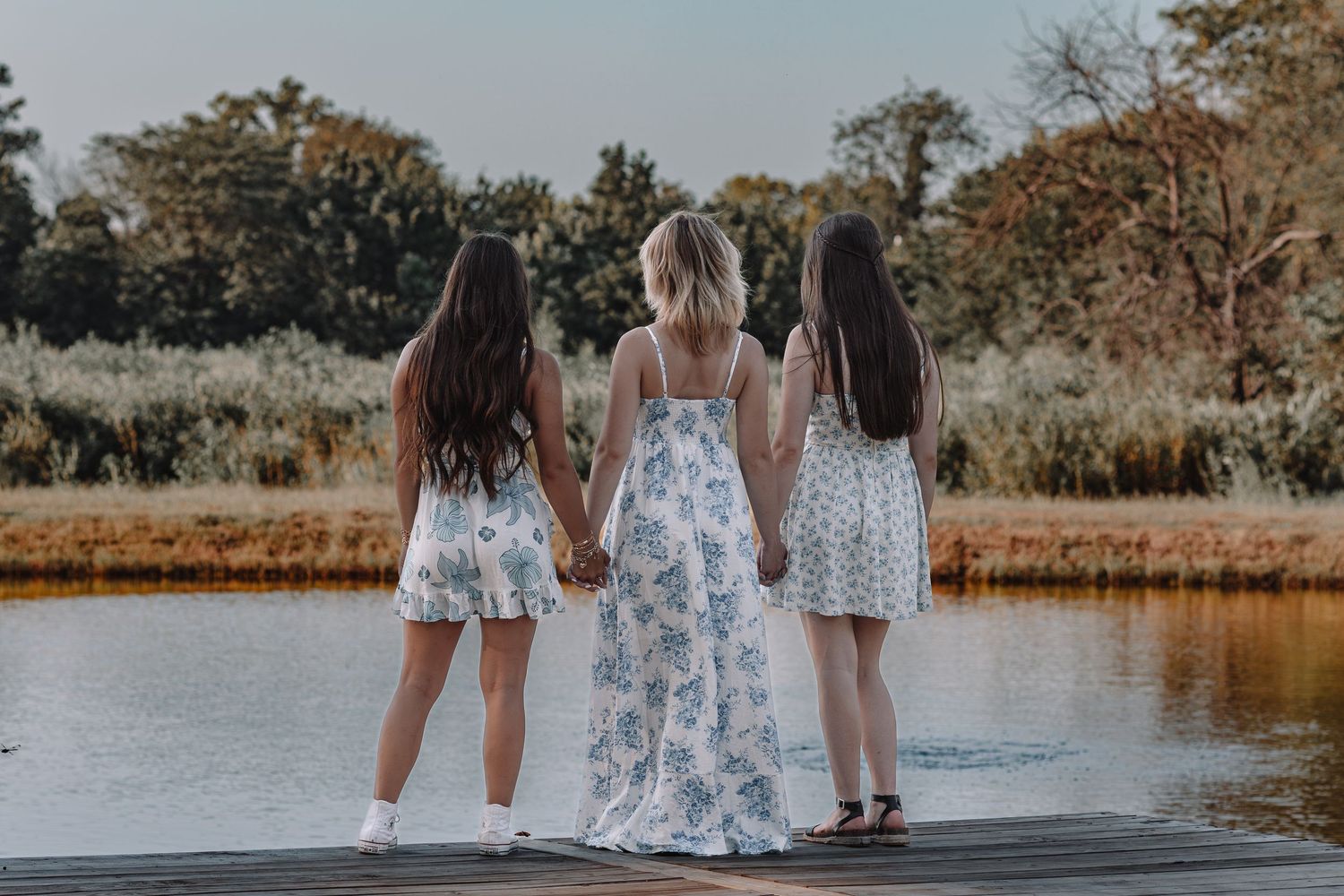 People in summer dresses standing near a tranquil waterfront at sunset.