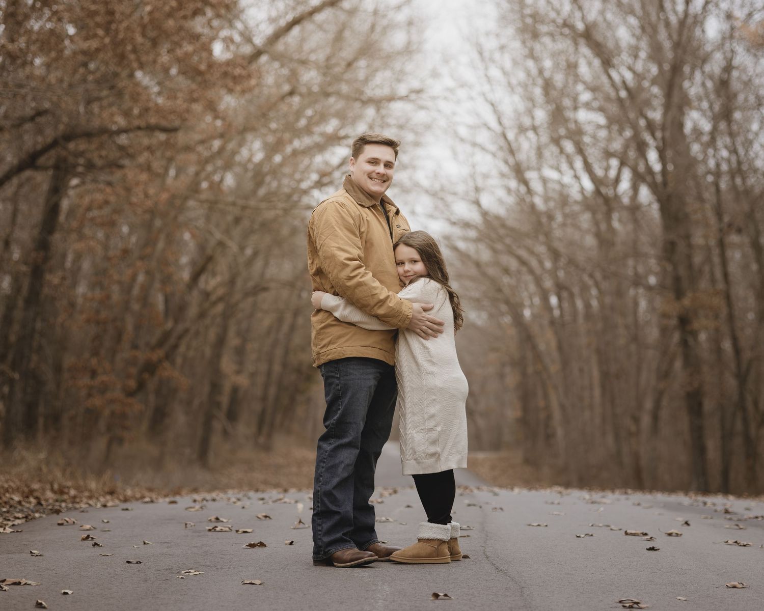 A couple embraces on a path surrounded by bare autumn trees in a romantic outdoor photoshoot.