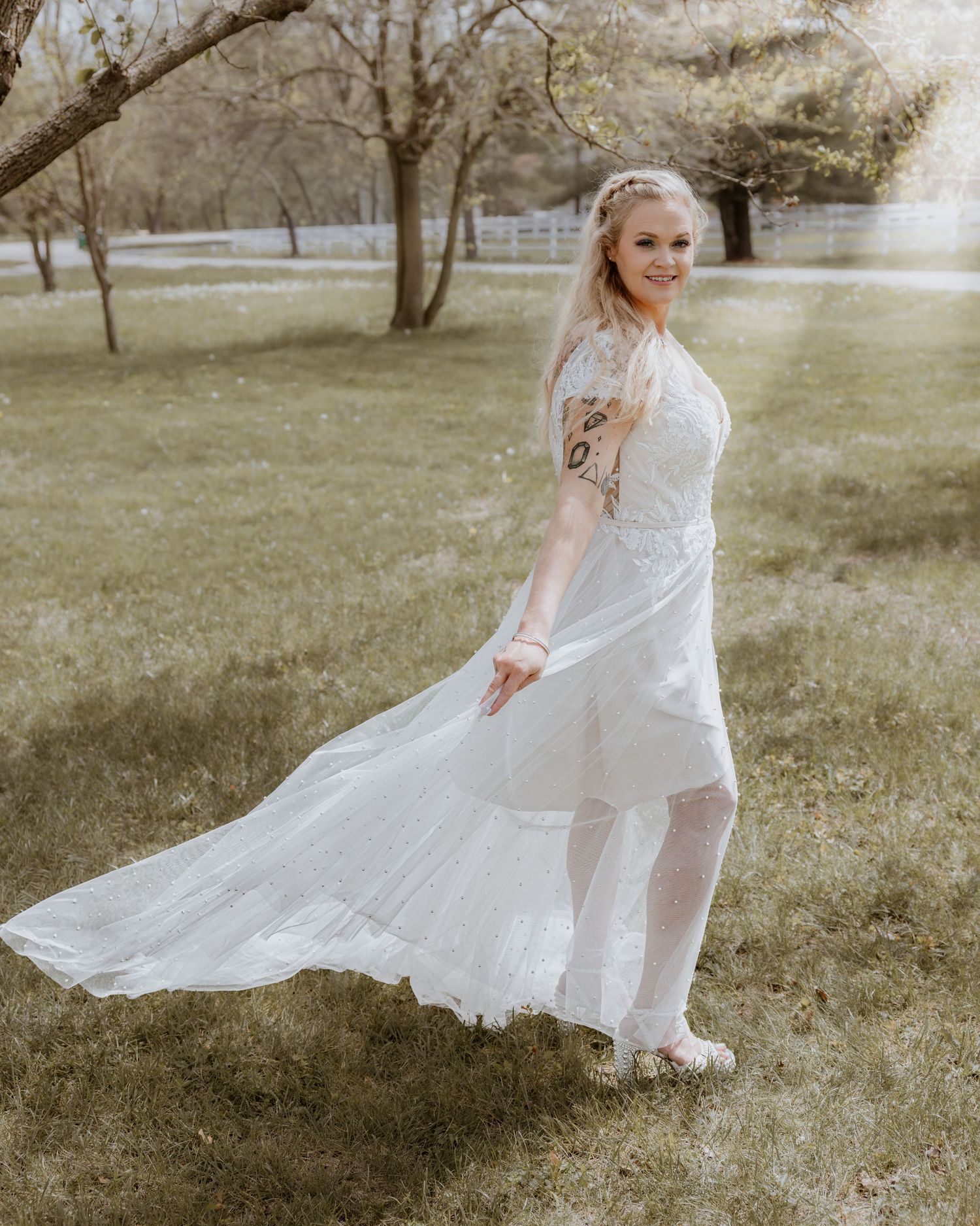 Bride twirling in flowing white lace wedding gown in a green outdoor garden setting.
