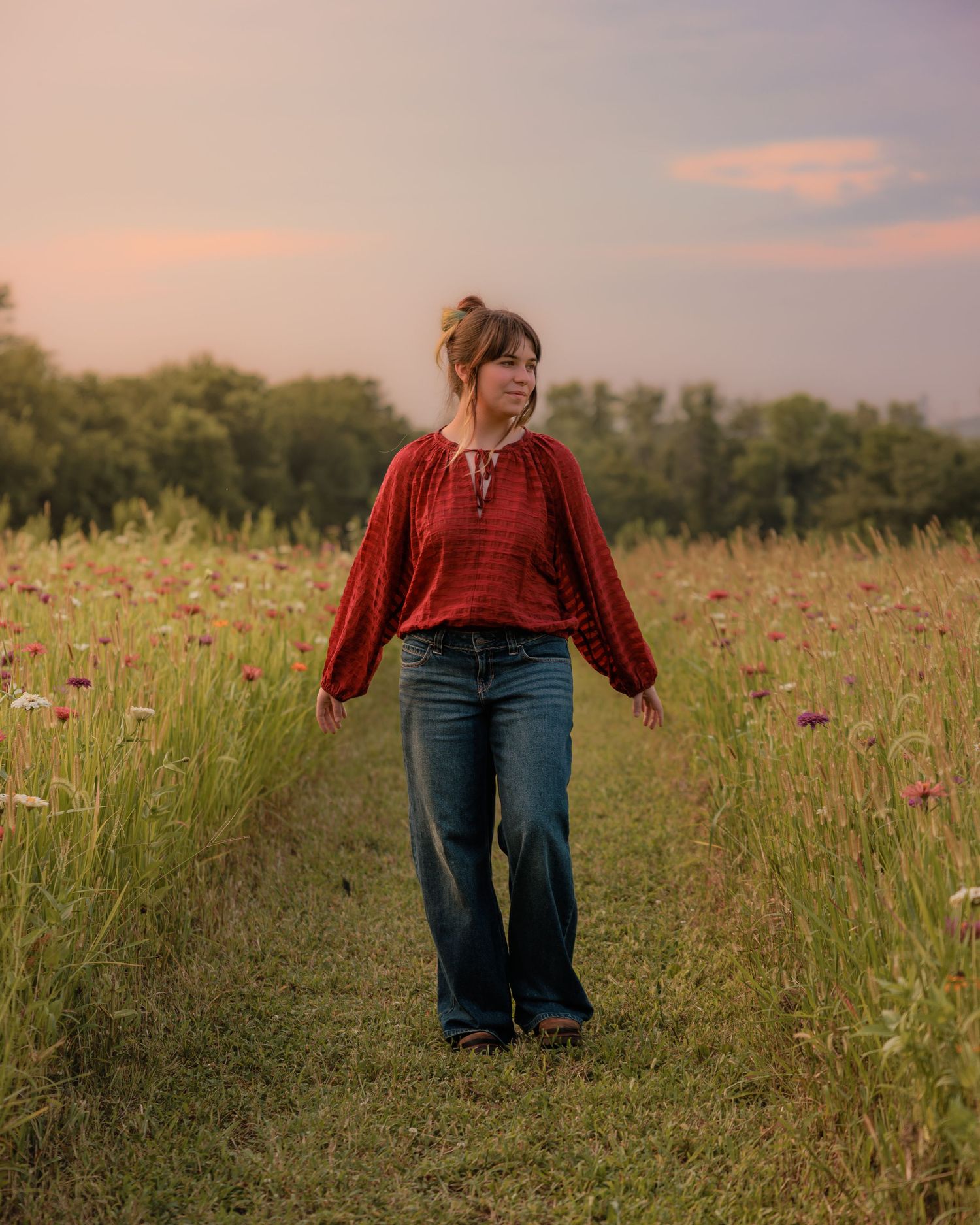 Woman in red blouse and wide-leg jeans walking through a wildflower meadow at sunset.