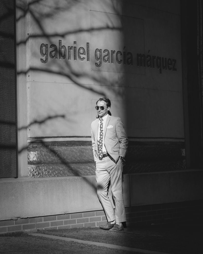 A person in a light colored suit stands against a wall with Gabriel Garcia Marquez text in black and white.
