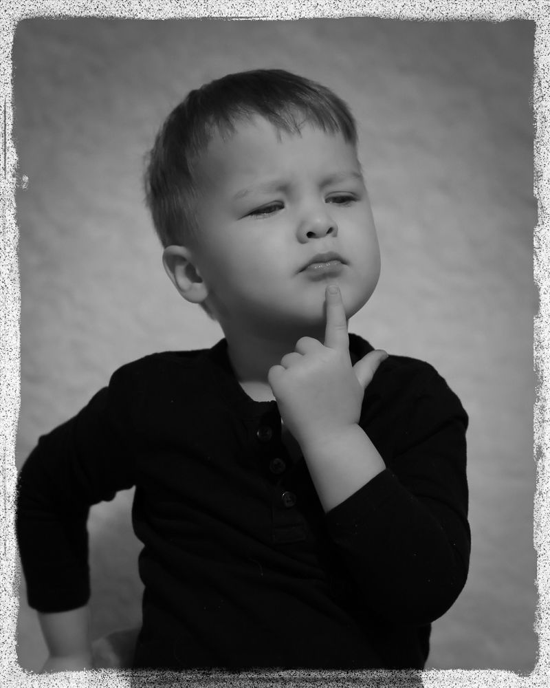 Black and white photo series showing a child in dark clothing making expressive faces against a light background.