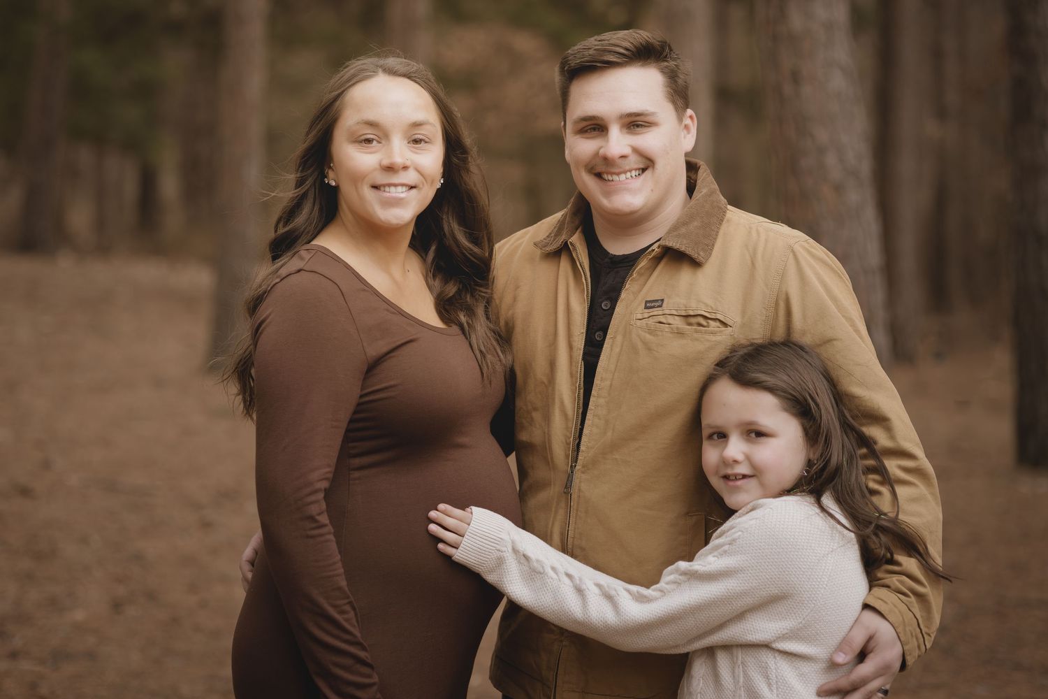 A family poses together in a forest setting wearing brown and tan coordinated outfits during an outdoor photo session.