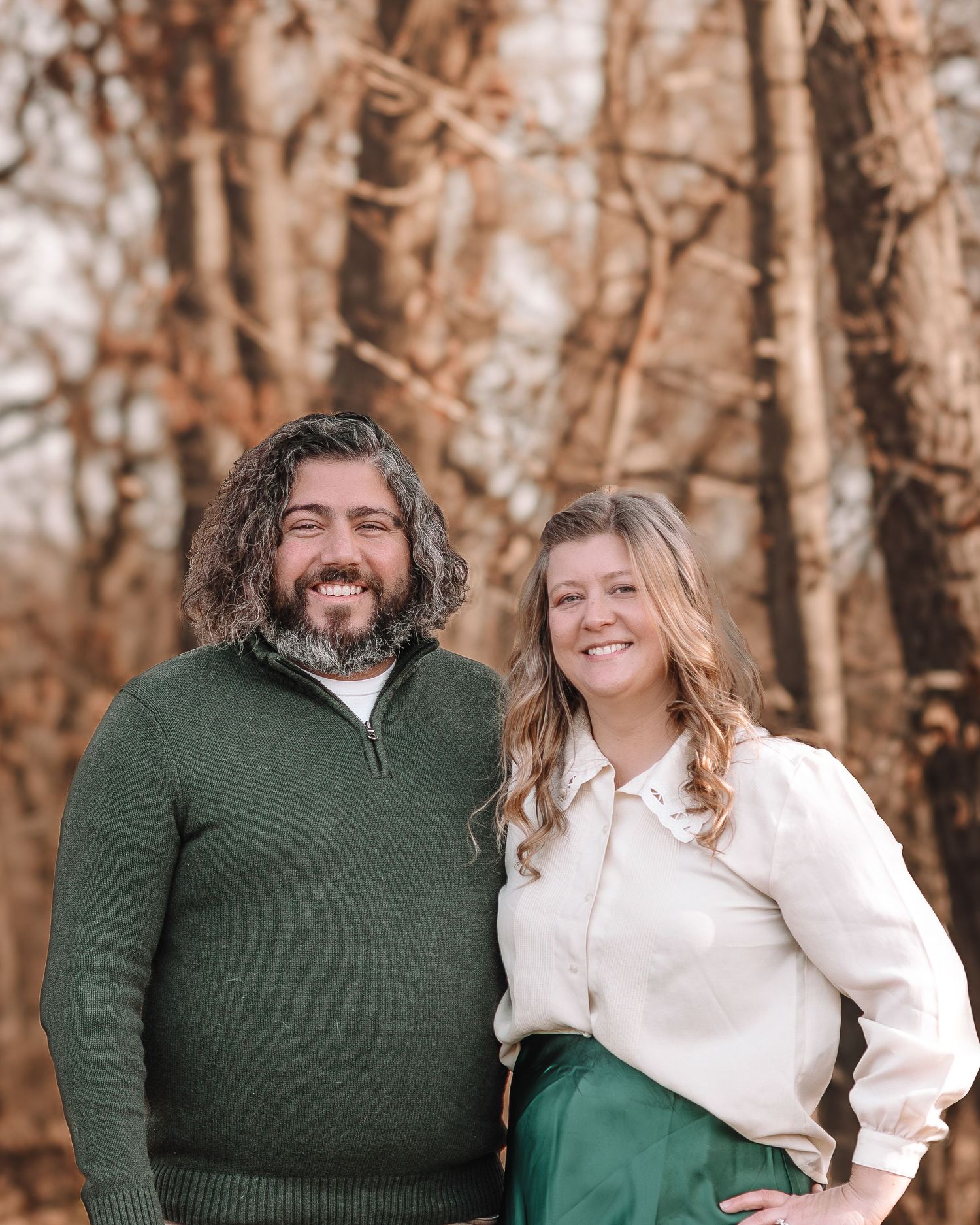 A couple in green sweater and white shirt share joyful moments together in a forest setting with autumn trees.